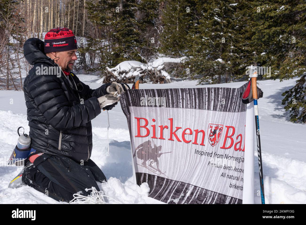 L'uomo si inginocchia nella neve mentre mette in su un segno che fa pubblicità ad una corsa di sci di fondo ispirata Berkenbeiner nel Chama Ski Classic vicino a Chama, NM. Foto Stock