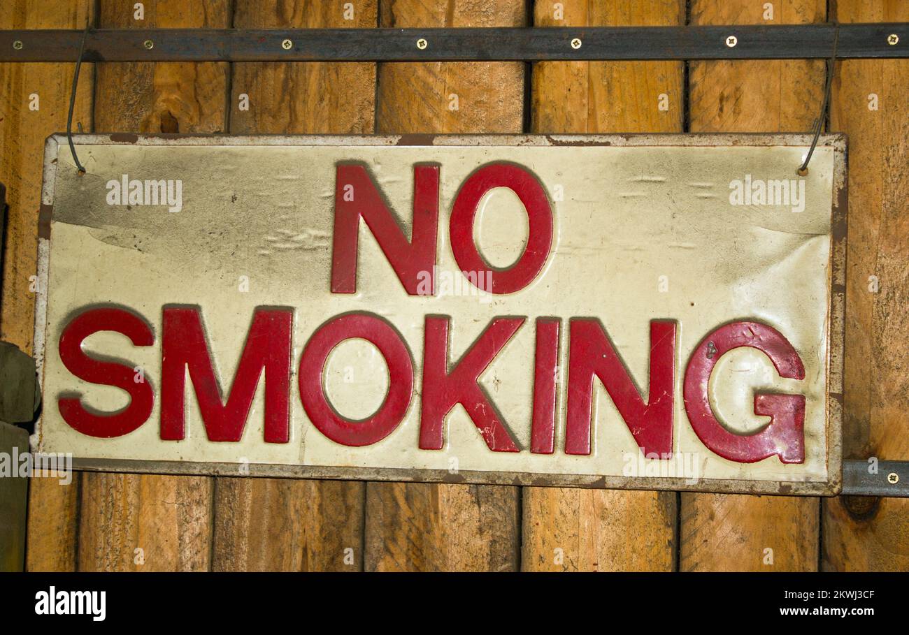 Segno ben indossato che mostra le parole No Smoking in lettere rosse su sfondo bianco contro una parete di legno Foto Stock