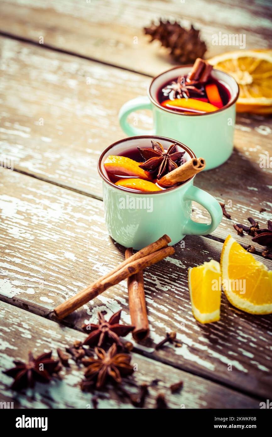 VIN brulé in tazze rustiche con spezie e agrumi su fondo in legno Foto Stock