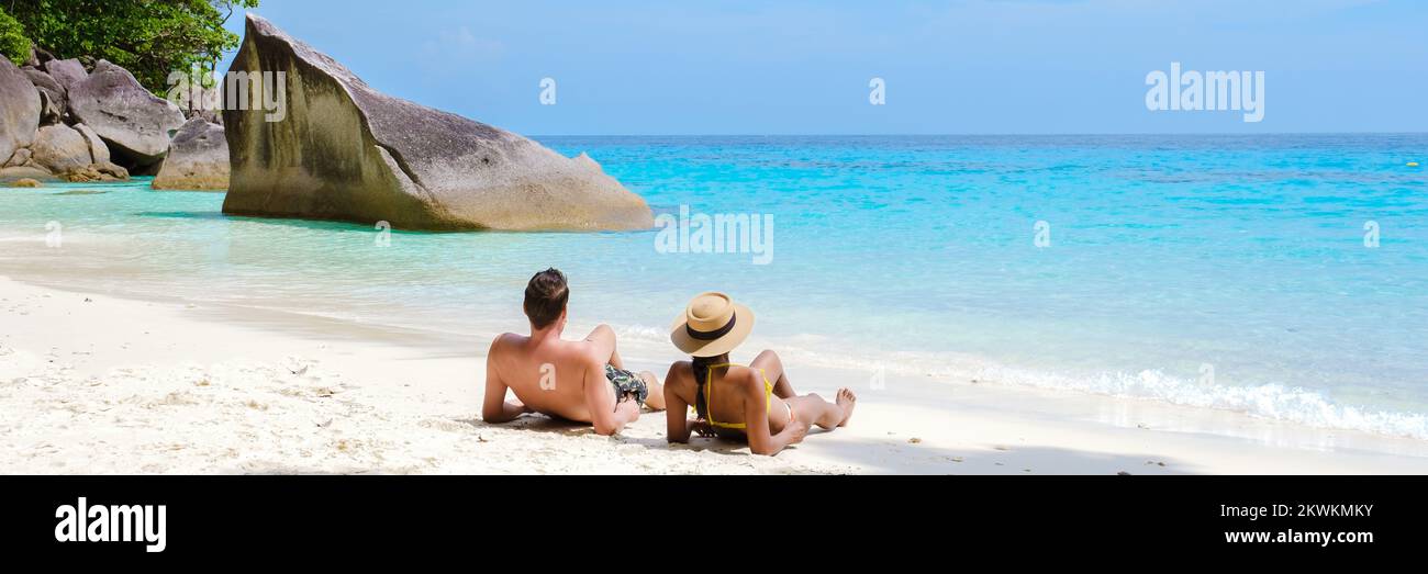 Un paio di uomini e donne che si adagiano sulla spiaggia bianca tropicale con l'oceano color serra delle Isole Similan Thailandia. Foto Stock