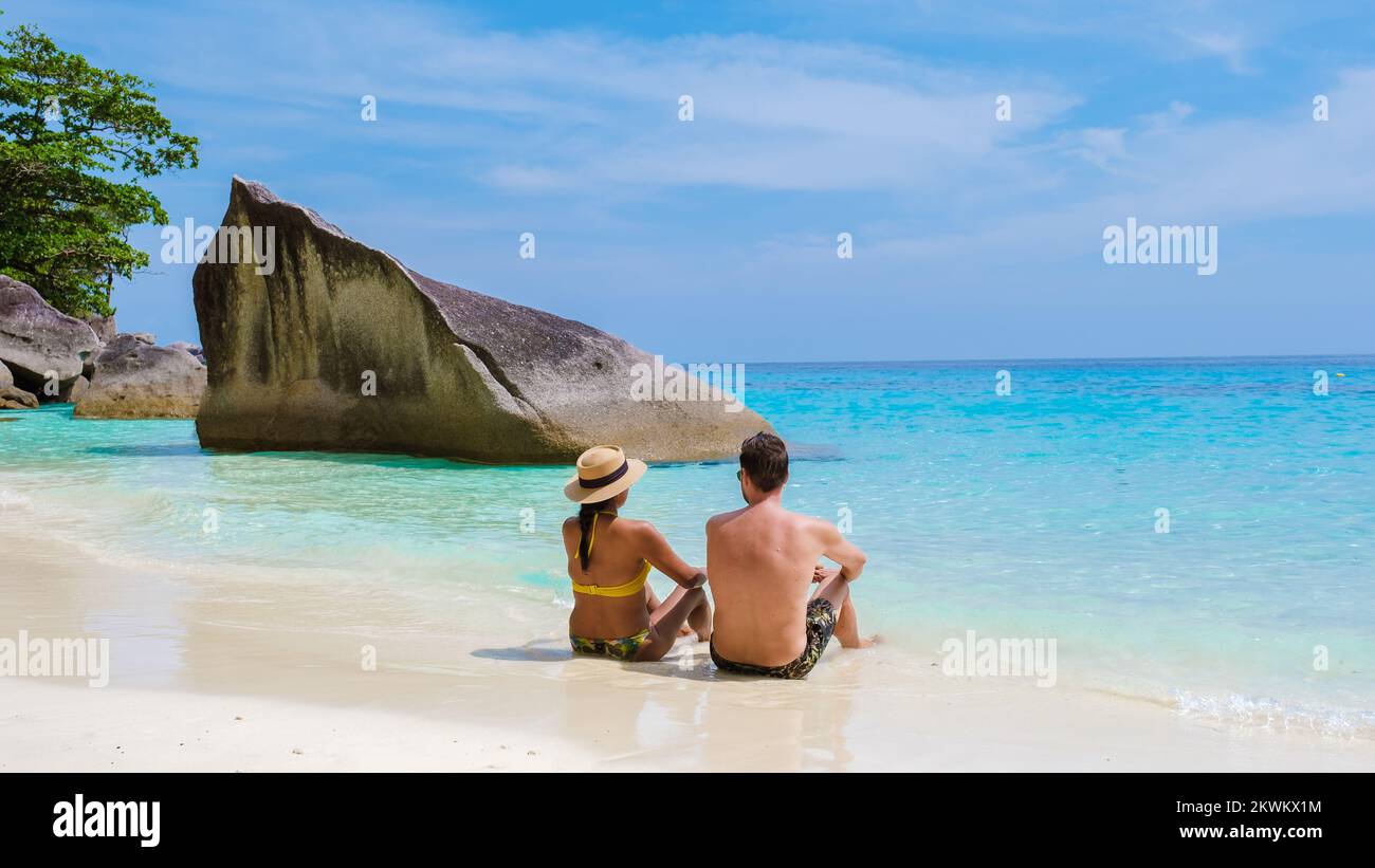 Un paio di uomini e donne che si rilassano prendendo il sole sulla spiaggia bianca tropicale con l'oceano colorato di serra delle Isole Similan Thailandia. Foto Stock