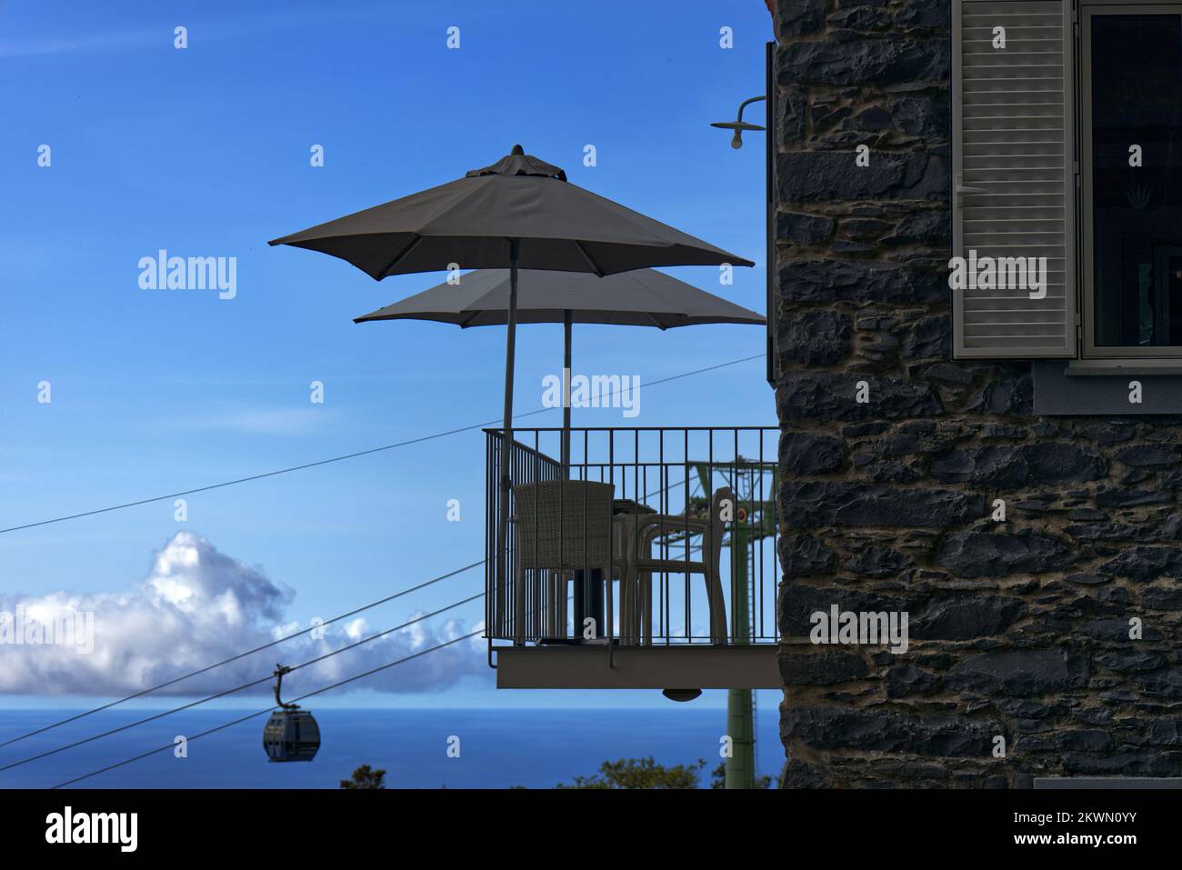 Funchal, isola di Madeira, Portogallo - ombrelloni sul balcone alto caffè a Monte con funivia che si avvicina alla stazione della funivia sullo sfondo Foto Stock
