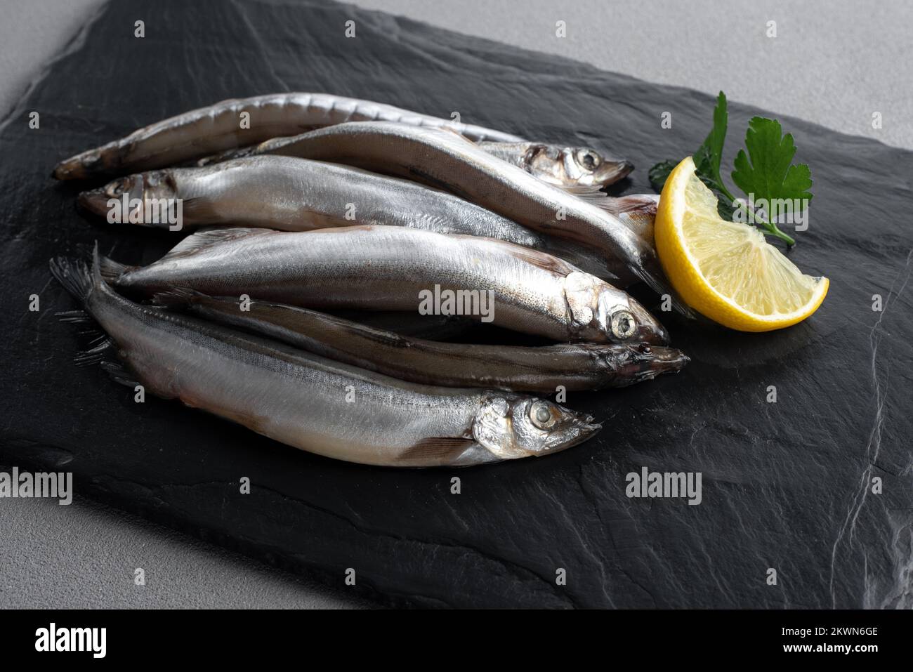Capelin di pesce fresco crudo con limone. Sfondo grigio. Vista dall'alto. Foto Stock