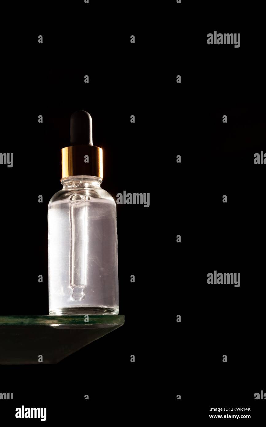 Olio essenziale naturale o siero in bottiglia di vetro su un podio di vetro. Spazio di copia. Sfondo nero Foto Stock