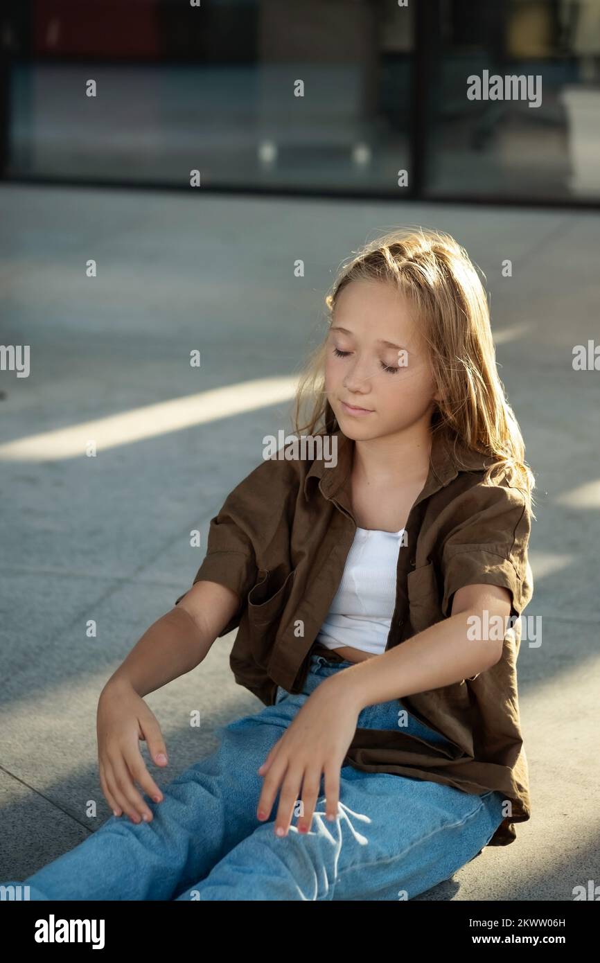 Ritratto creativo della ragazza adolescente seduta sul pavimento, strada urbana, luce del sole, mani in su Foto Stock