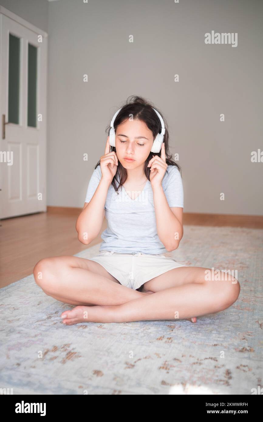 Ragazza giovane e graziosa che ascolta musica con le cuffie mentre si è in moquette a casa. Appartamento soggiorno. Vita domestica Foto Stock