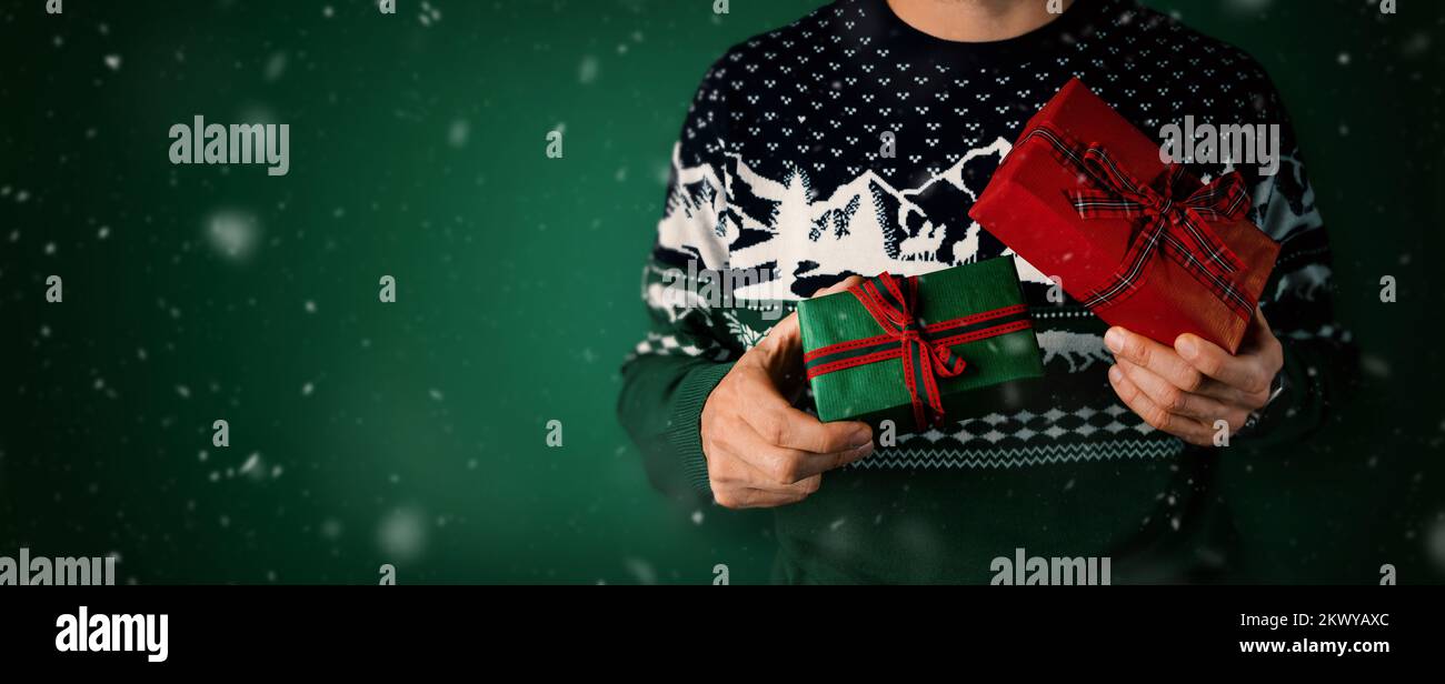 uomo in maglione di natale che tiene confezioni regalo imballate in mani su sfondo verde. banner con spazio di copia Foto Stock