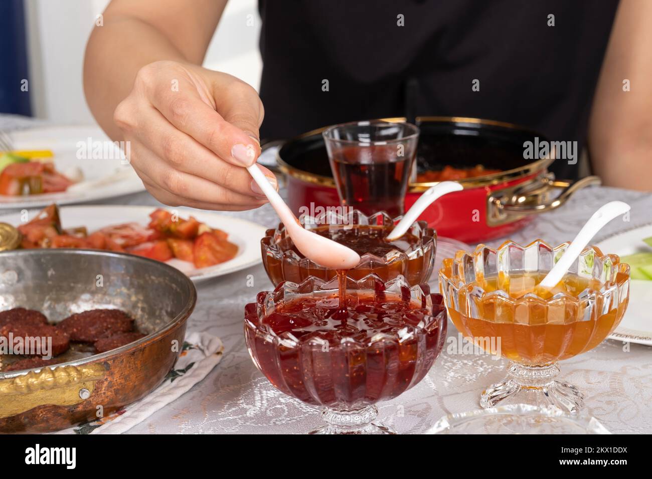 Confettura di fragole, donna caucasica che tiene il cucchiaio per prendere qualche confettura di fragole. Tradizionale, delizioso e ricco tavolo per la colazione turco. Tè in vetro. Foto Stock