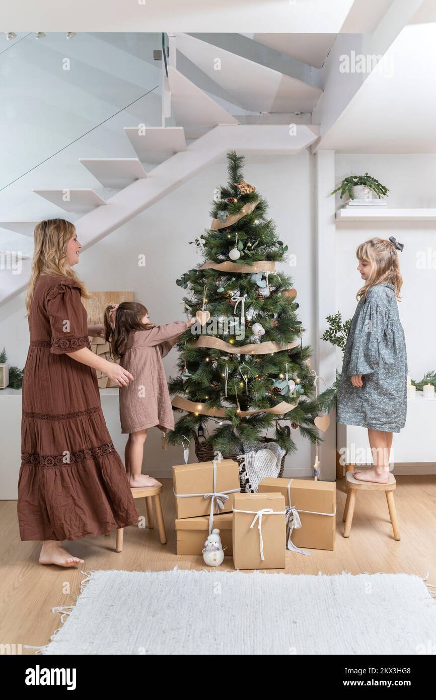 Due ragazze con la loro madre che decorano l'albero di natale nel loro soggiorno Foto Stock