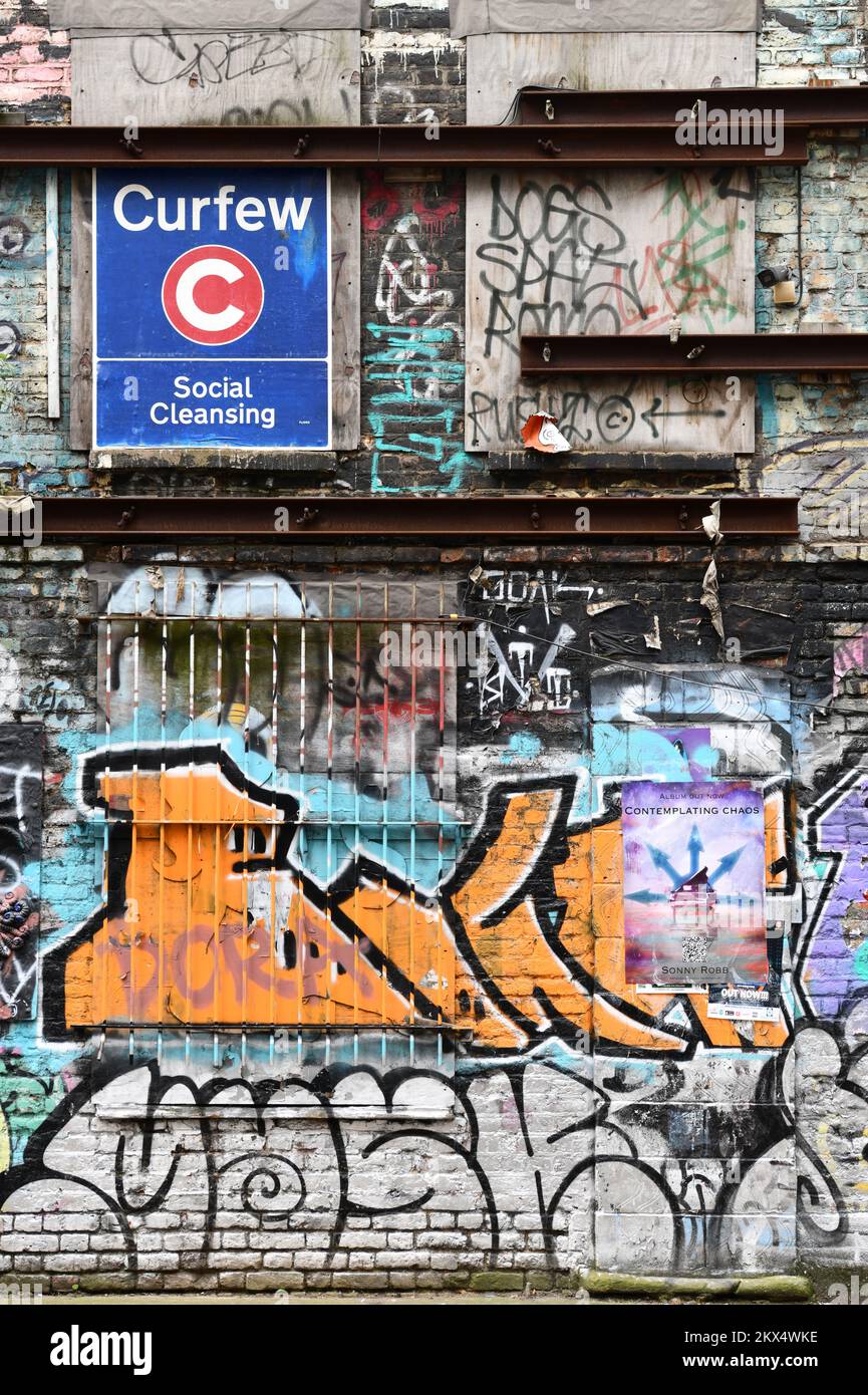 Muro con graffiti e segno con coprifuoco e pulizia sociale a Shoreditch, Londra Foto Stock