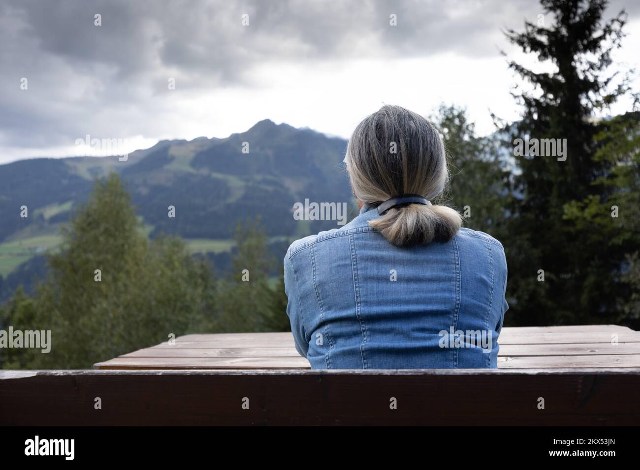 Una donna dai capelli grigi si siede su una panca tutta da sola. Foto Stock