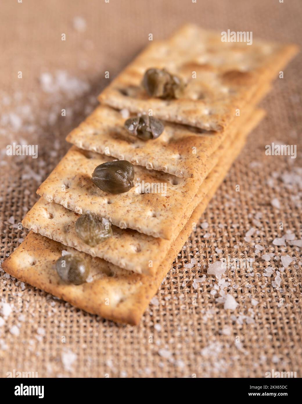 Alcuni cracker integrali sono impilati come una scala, con capperi e sale di roccia sopra e intorno Foto Stock