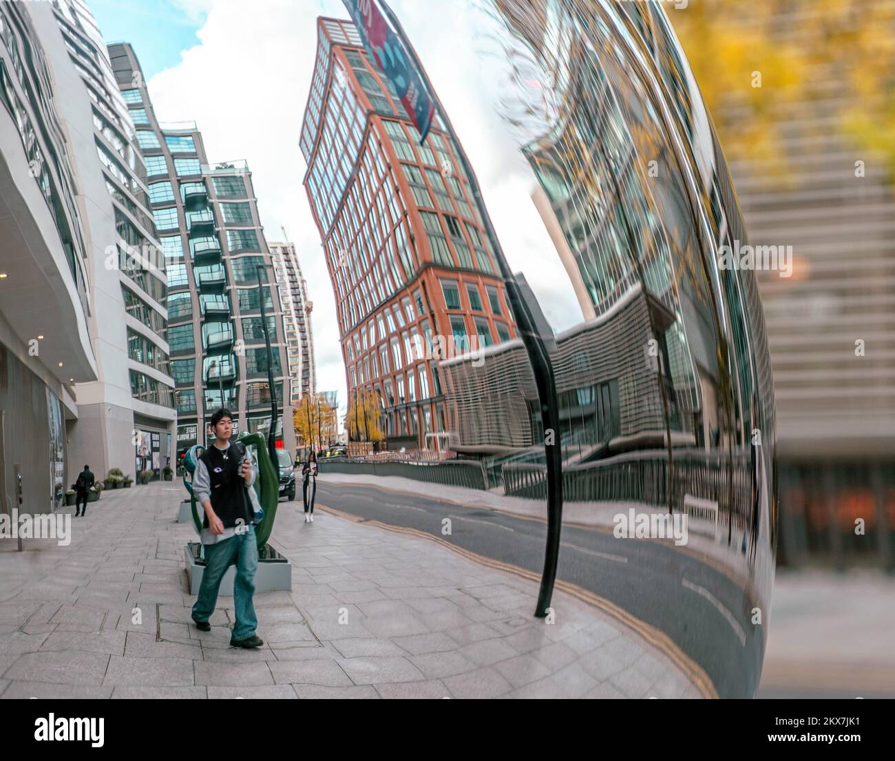 Riflesso distorto dall'opera d'arte The Knot, di un giovane uomo che cammina e dei raschietti curvi sullo sfondo di Water Street, Canary Wharf, East London. Foto Stock