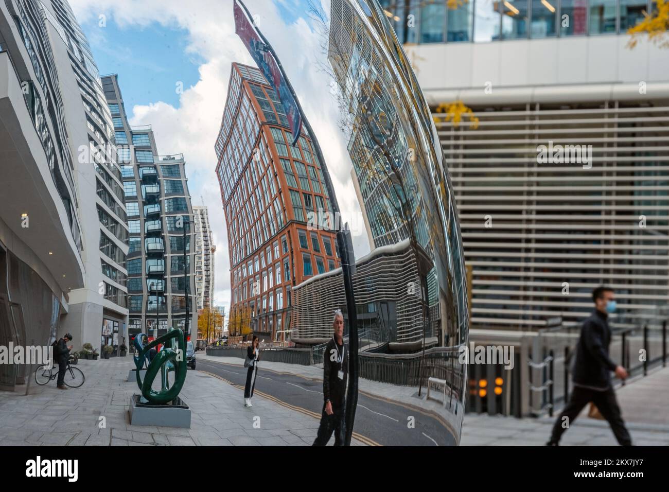 Riflesso distorto dall'opera d'arte The Knot, di persone che camminano e curvano i raschietti sullo sfondo di Water Street, Canary Wharf, East London. Foto Stock