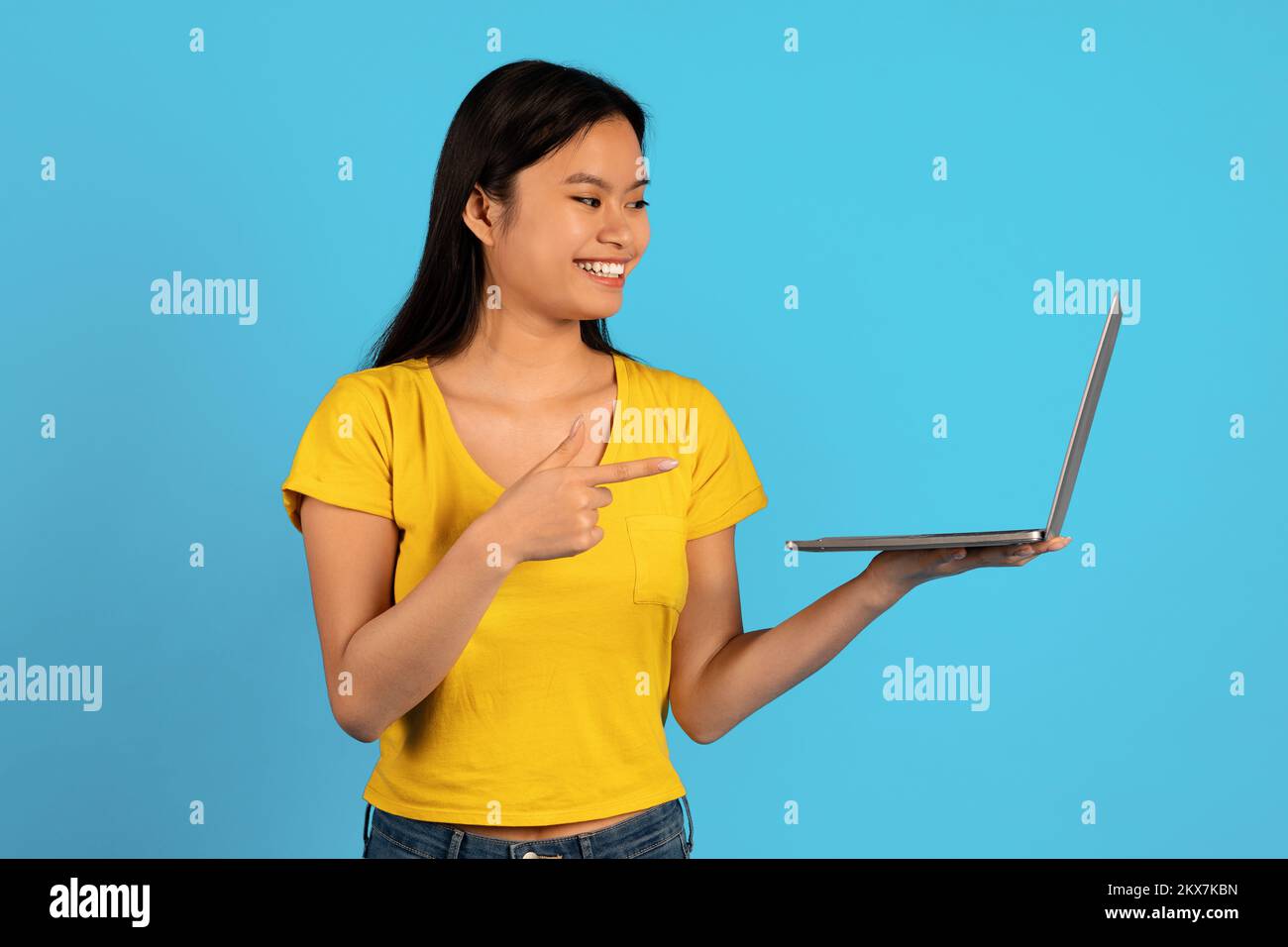 Annuncio e offerta, vendita enorme. Felice giovane studentessa asiatica in t-shirt gialla punto dito sullo schermo del computer Foto Stock