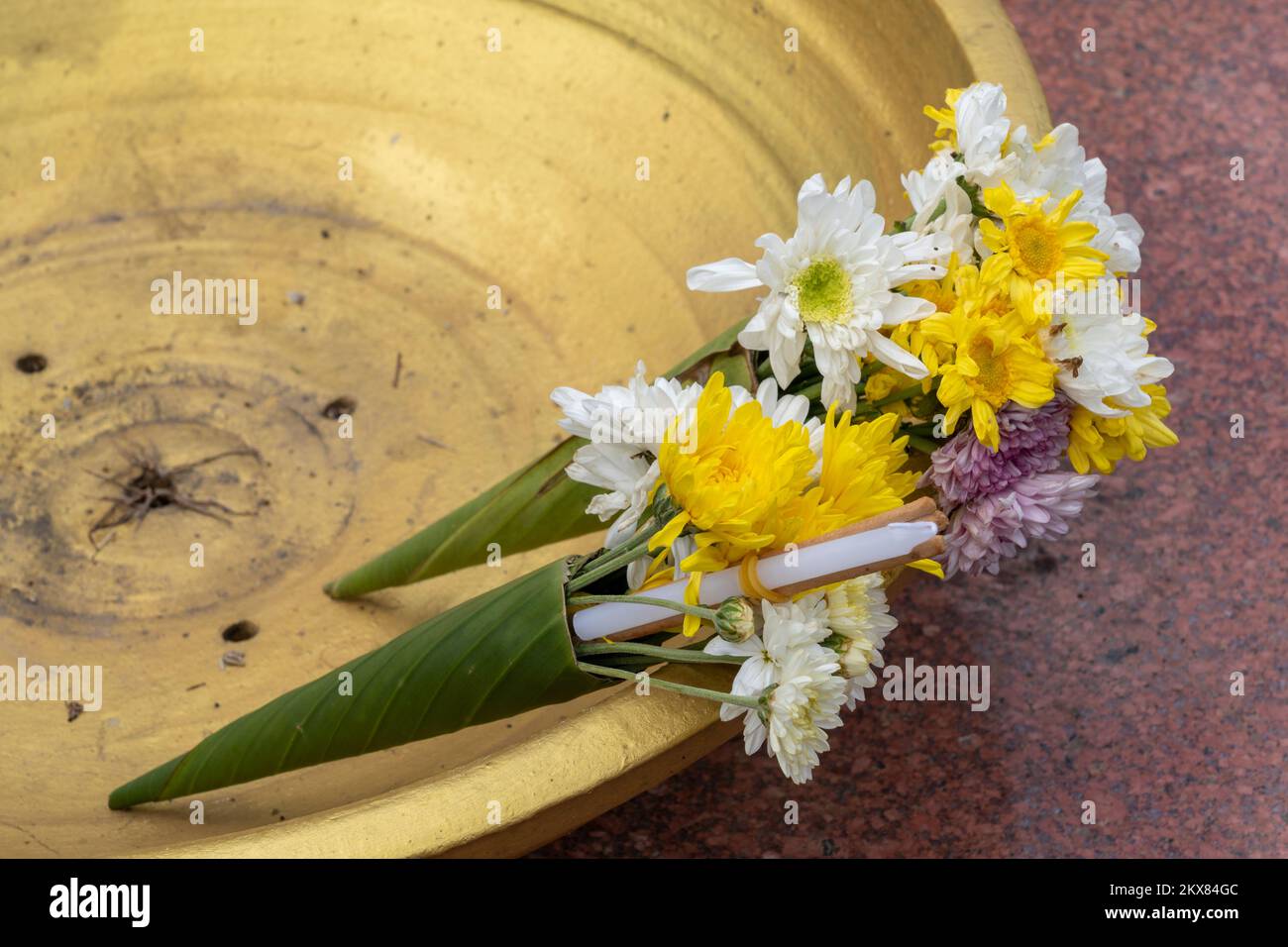 Offerte tradizionali di fiori di crisantemo, candele e bastoni di incenso in coni di foglia di banana incastonati in una ciotola d'oro nel tempio buddista, Thailandia Foto Stock