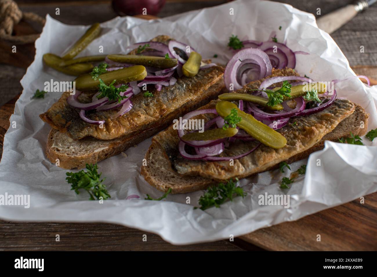 Aringhe fritte con cipolle rosse, sottaceti su pane di segale imburrato e tostato su tavola di legno Foto Stock