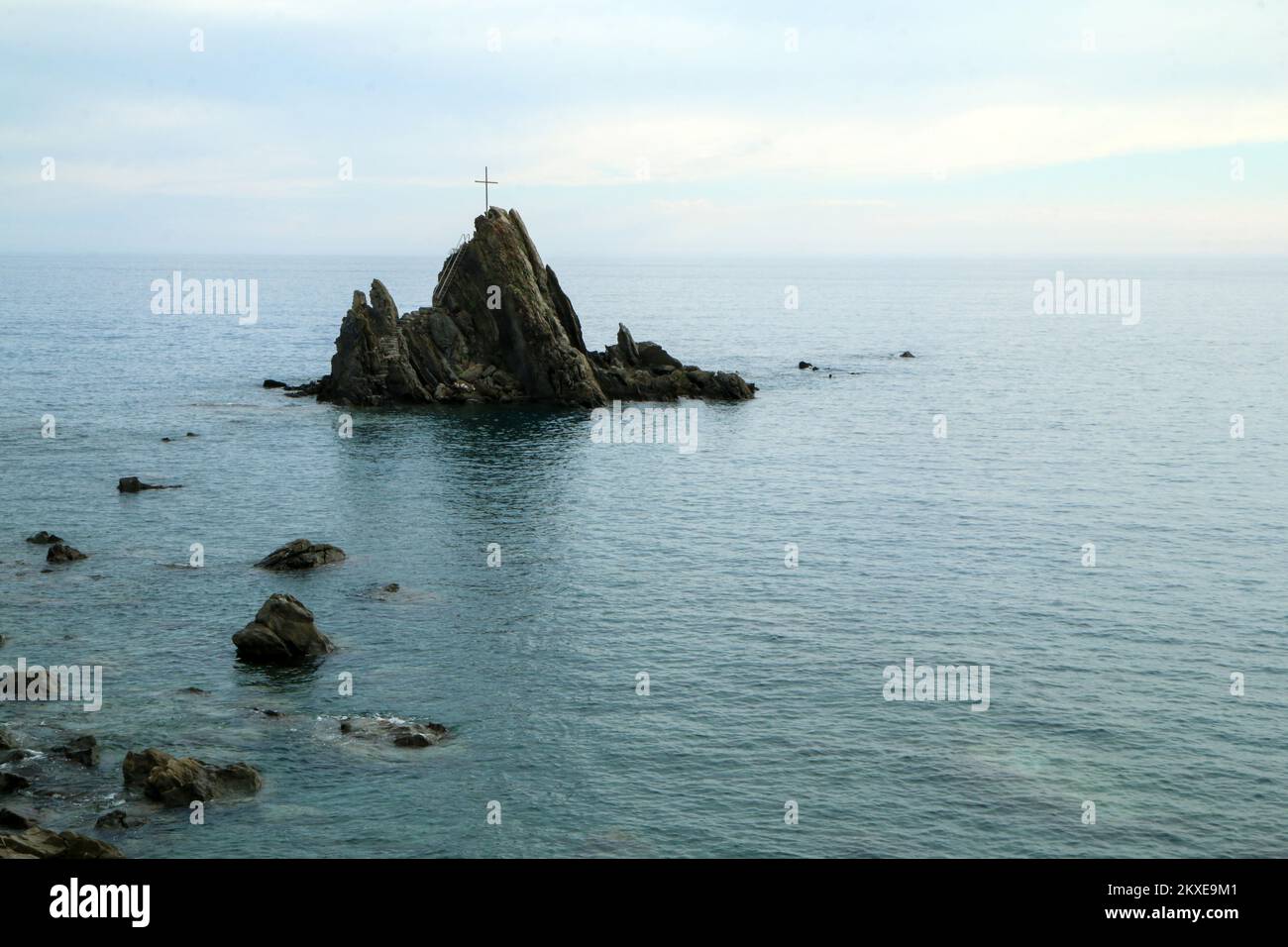L'isola solitaria rocciosa con una semplice croce in cima alla costa in Italia nei pressi di Sestri Levante nel tardo pomeriggio estivo. Foto Stock