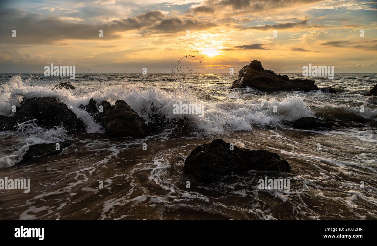 Un'onda dell'oceano sta rompendo contro Un cielo colorato del tramonto in formato immagine ad alta risoluzione Foto Stock