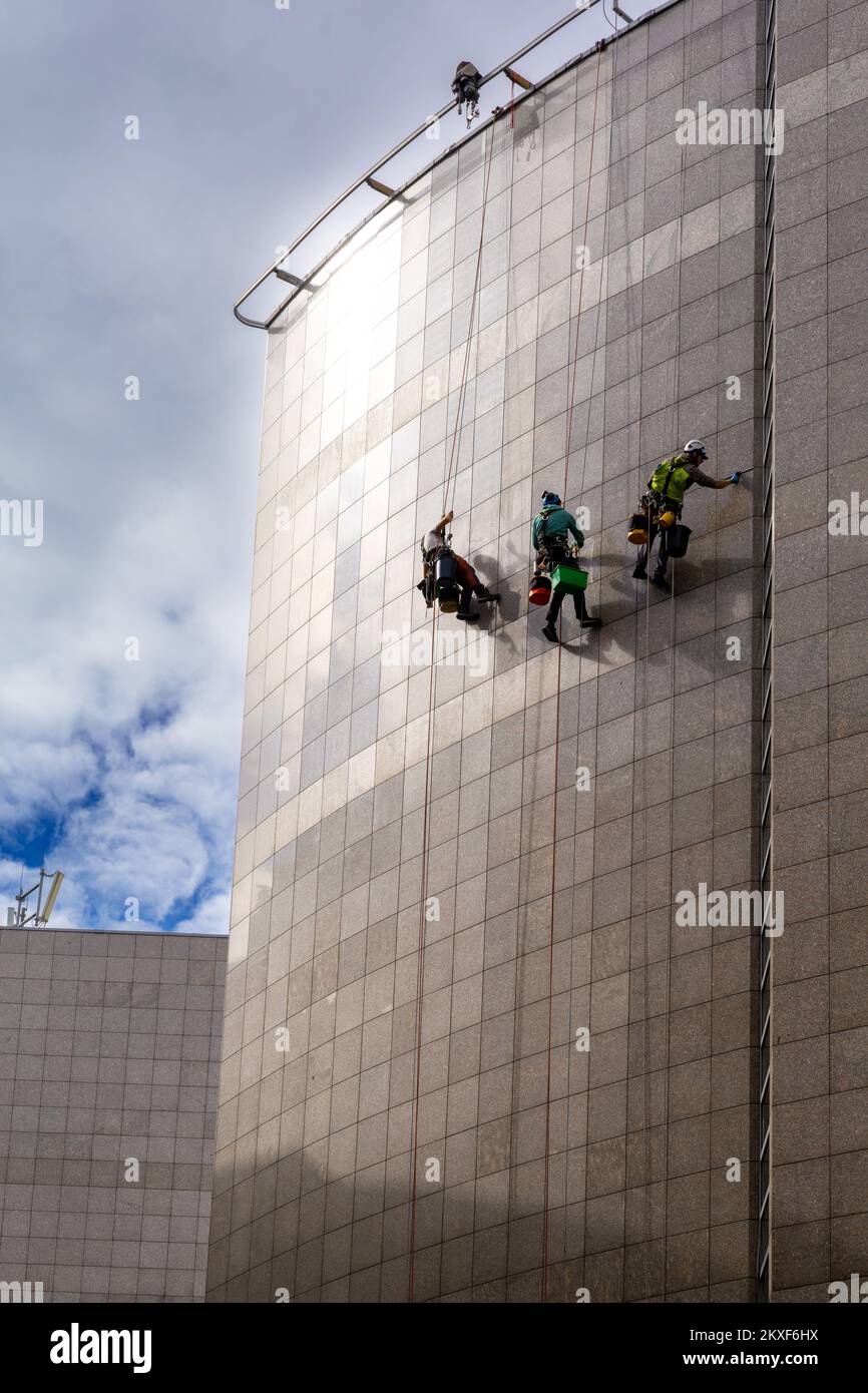 Budapest, Ungheria - 4 ottobre, 2022: Tecnici di accesso a funi appesi sul lato di un alto edificio in metallo e che puliscono la facciata Foto Stock