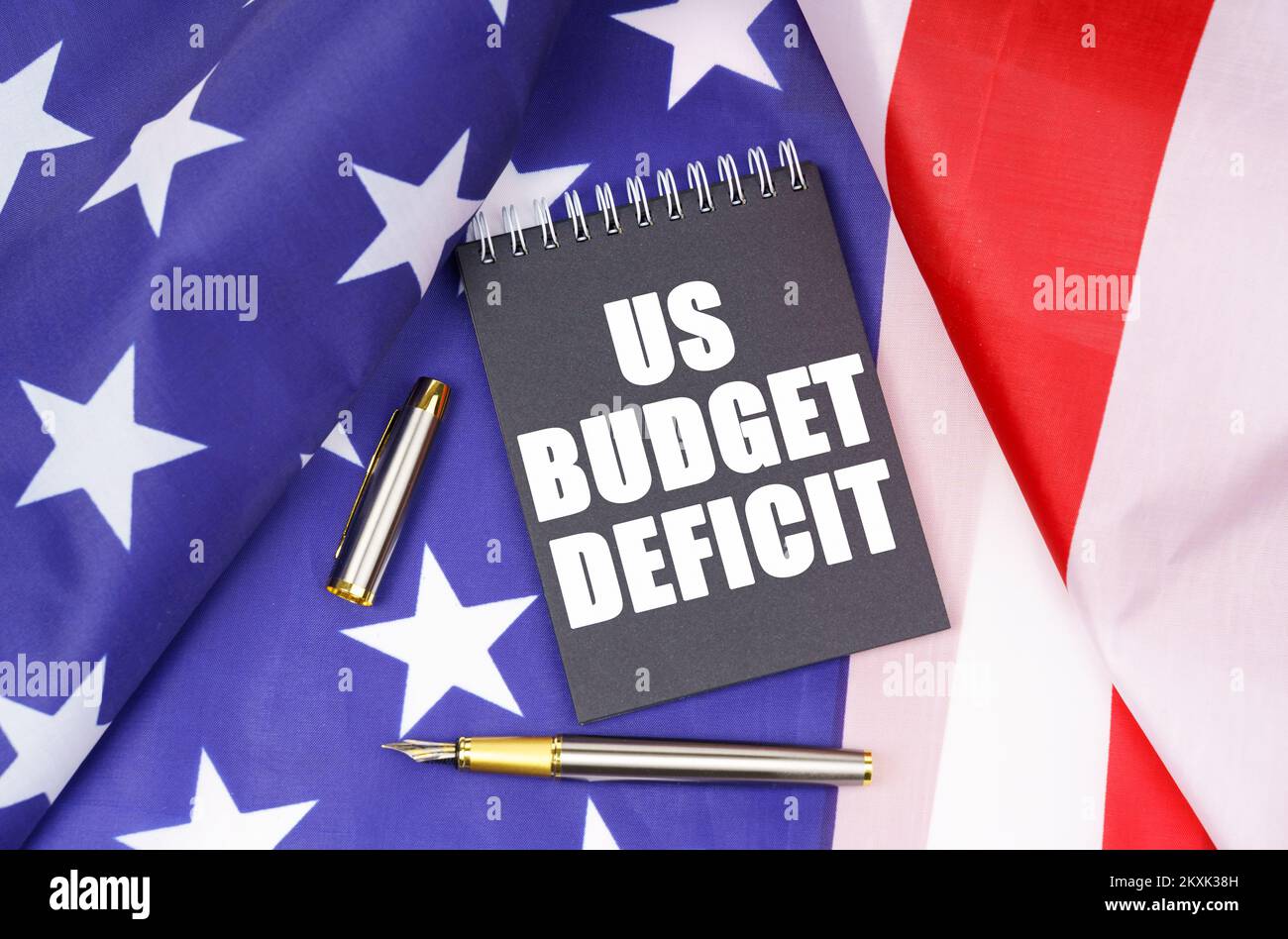Concetto aziendale. Sulla bandiera americana si trova una penna e un quaderno con l'iscrizione - il deficit di bilancio degli Stati Uniti Foto Stock
