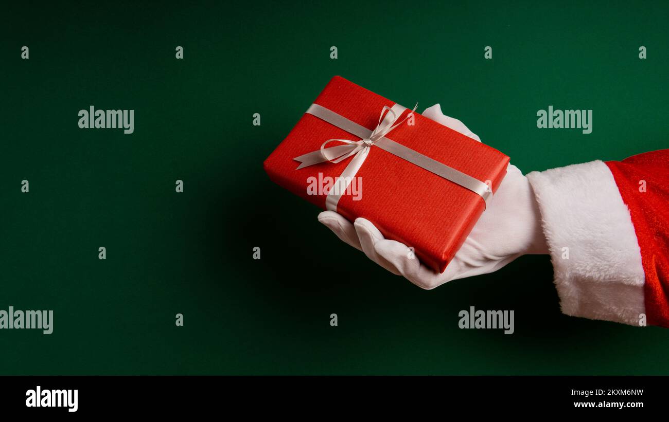 Mano di Babbo Natale tagliata che dà i regali contro sfondo verde Foto Stock
