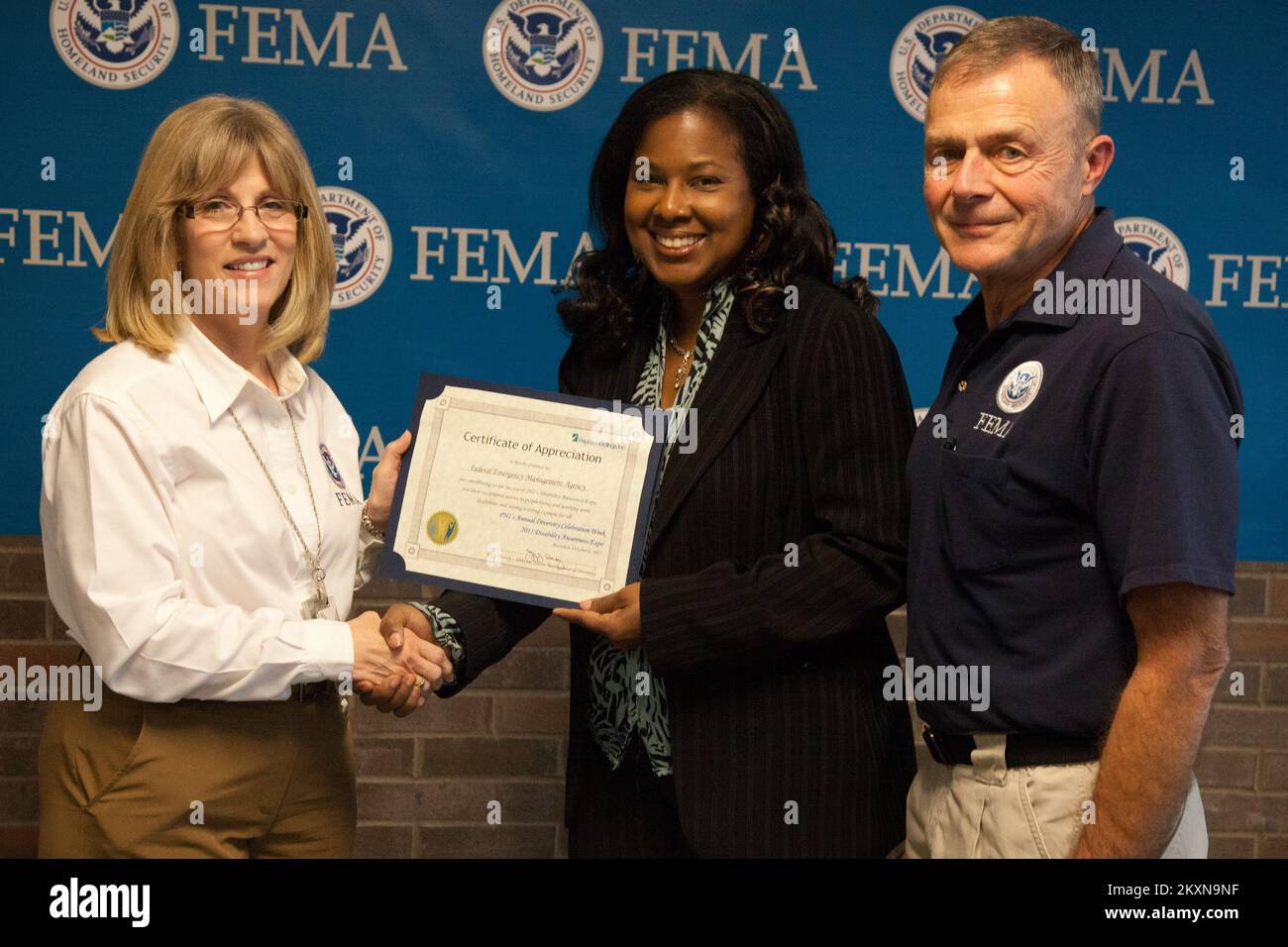 Inondazioni uragano/tempesta tropicale - Neptune, N. J., 16 novembre 2011 Sandra May (Center), Senior Media Representative for Atlantic City Electric, presenta un certificato di apprezzamento rilasciato a FEMA per aver contribuito al successo della fiera Disability Awareness Expo di Pepco Holdings Inc. La presentazione è stata effettuata al termine di un tour del settore privato dell'Ufficio comune sul campo della FEMA (JFO) a Nettuno. Il tour è stato condotto dal Coordinator Federale Bill Vogel (a destra) e Susan Langhoff (a sinistra), Assistente per gli Affari esterni del settore privato. La FEMA incoraggia il coinvolgimento della setta privata Foto Stock