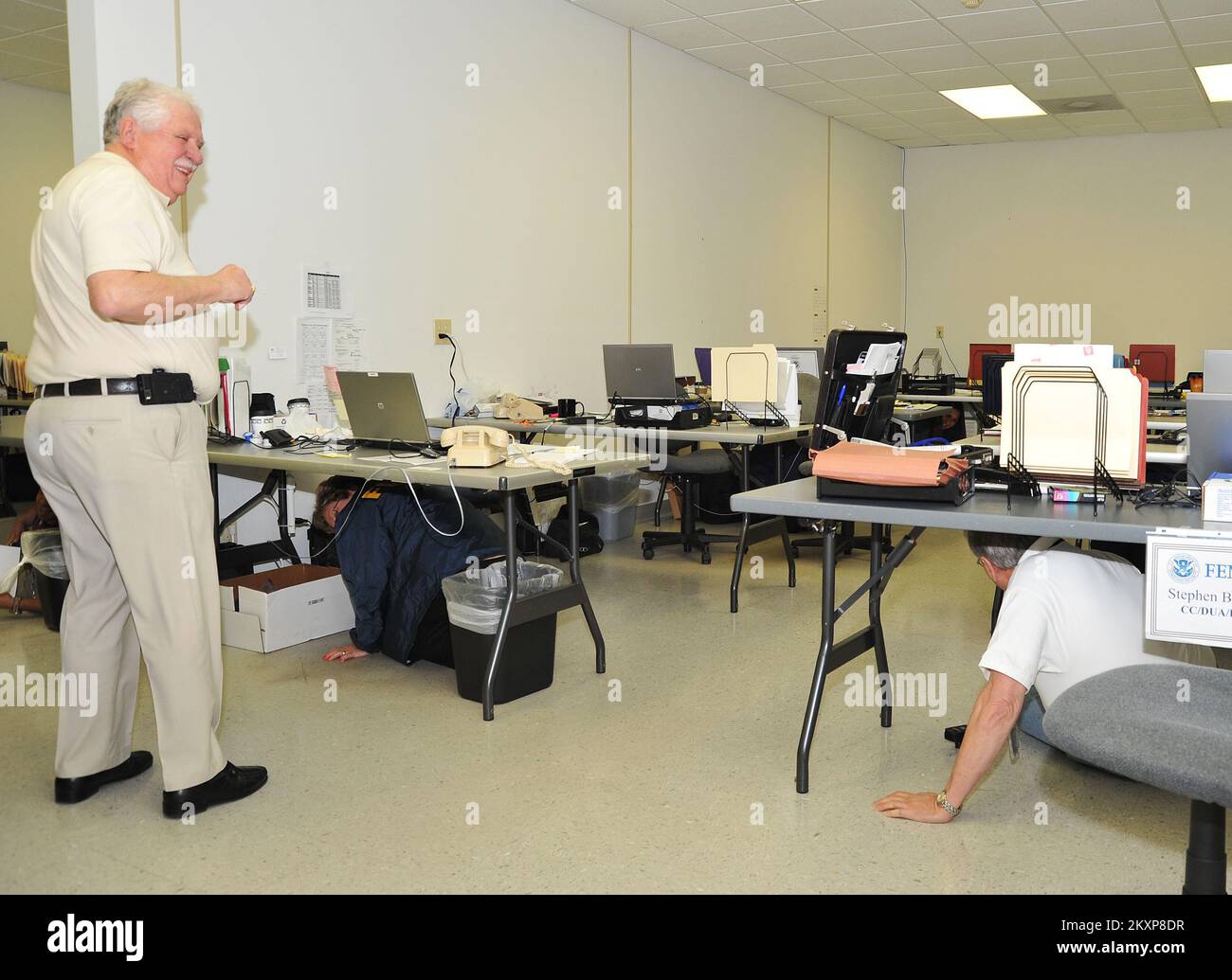 Grave tempesta del terremoto - Pelham, Ala. , 7 febbraio 2012 Hal Pashon, responsabile della sicurezza FEMA, guida lo shakeout nell'ufficio sul campo congiunto di Pelham, Alabama. Durante il trivello da terremoto a livello statale, i dipendenti cadono a terra, si coprono scendendo sotto una scrivania o un tavolo robusto e si tengono in mano fino a quando non si arresta l'agitazione. Il trapano mira a promuovere la preparazione al terremoto. . Alabama forti tempeste, tornado, Straight-Line Winds, e alluvioni. Fotografie relative a disastri e programmi, attività e funzionari di gestione delle emergenze Foto Stock
