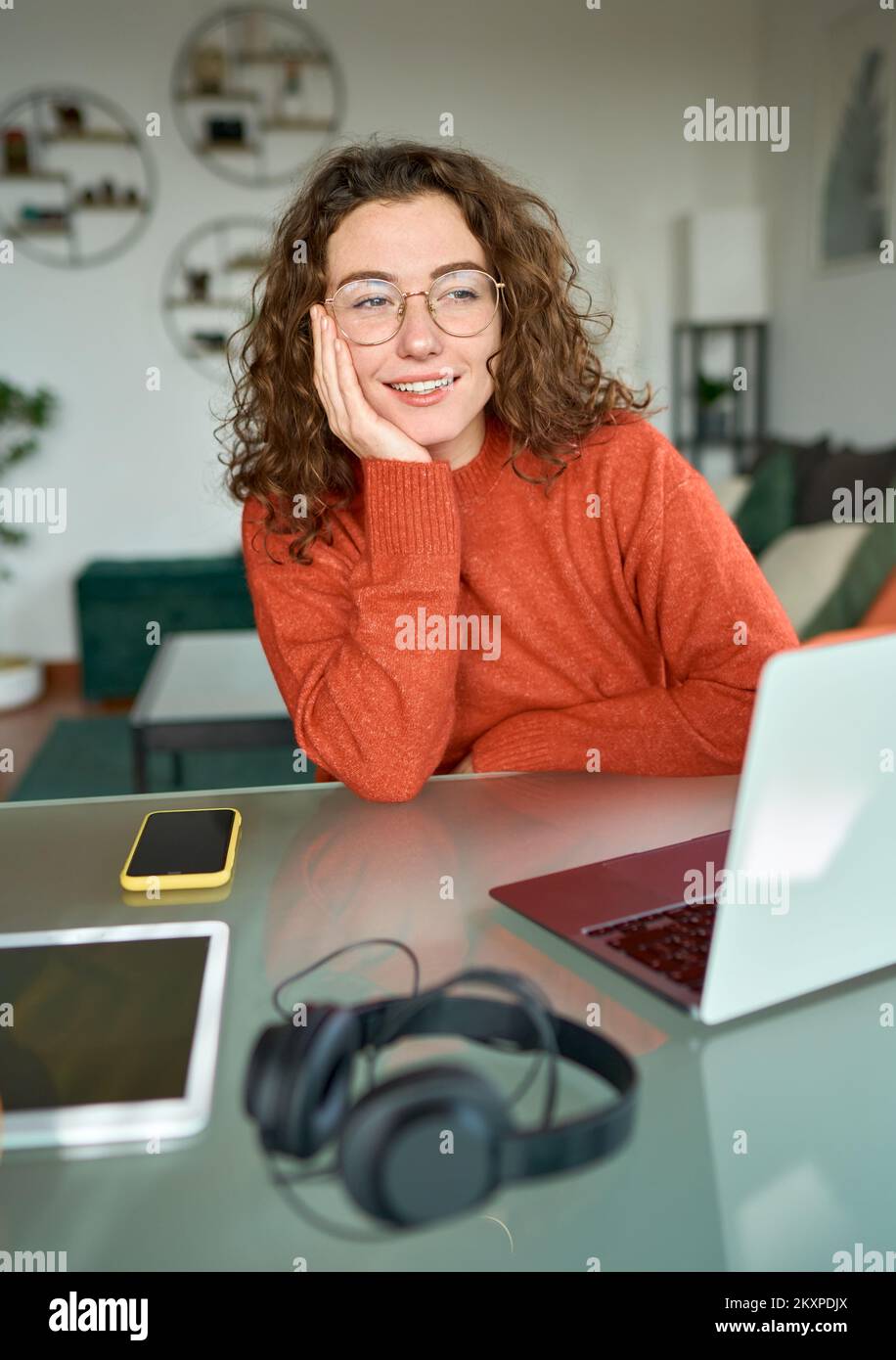Giovane donna felice che guarda lontano e pensa mentre lavora sul notebook a casa. Foto Stock