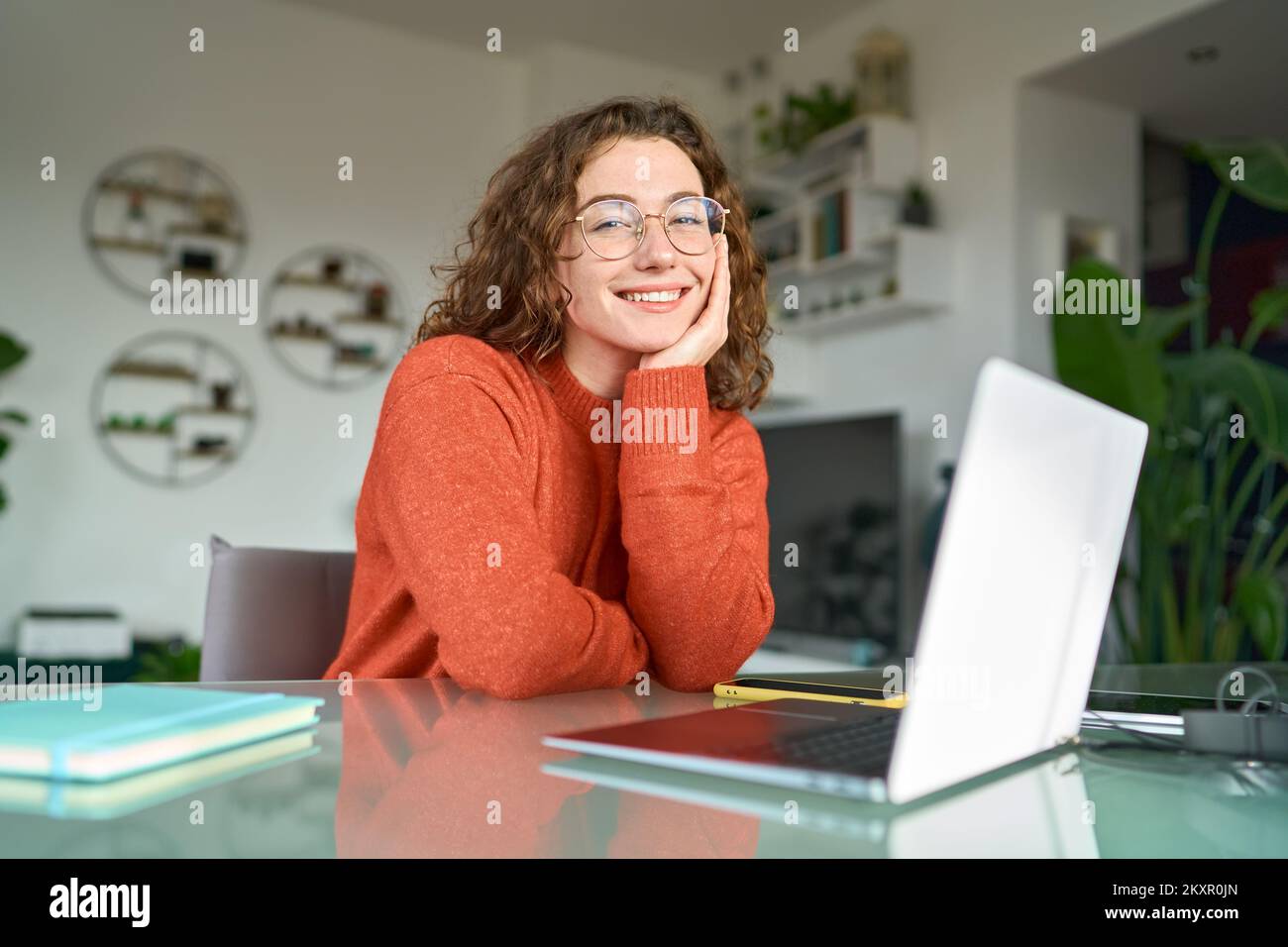 Giovane donna sorridente, graziosa studentessa seduta al tavolo in ufficio con un computer portatile. Foto Stock