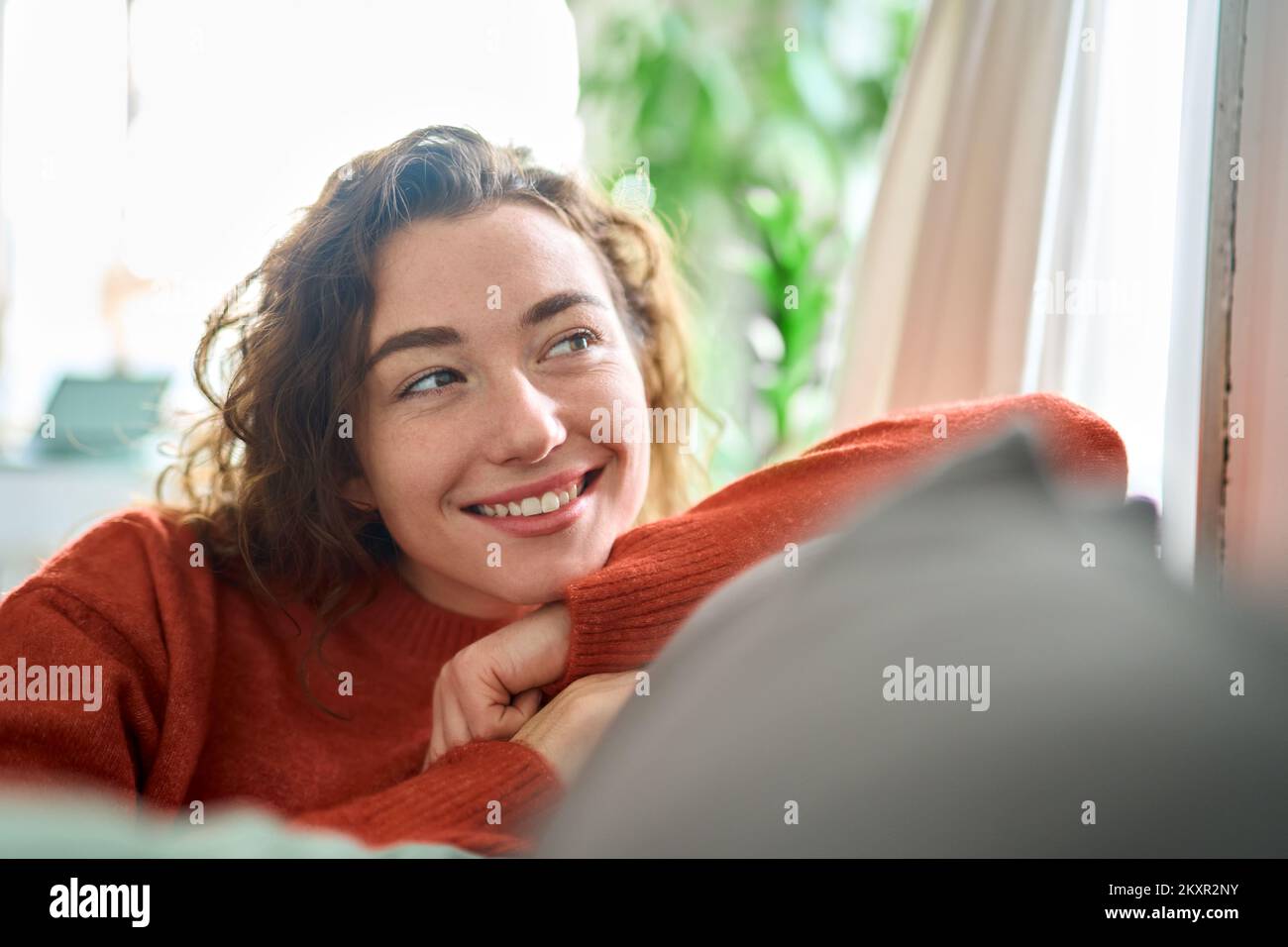 Giovane donna sognante felice che si rilassa seduto sul divano a casa, sognando. Foto Stock