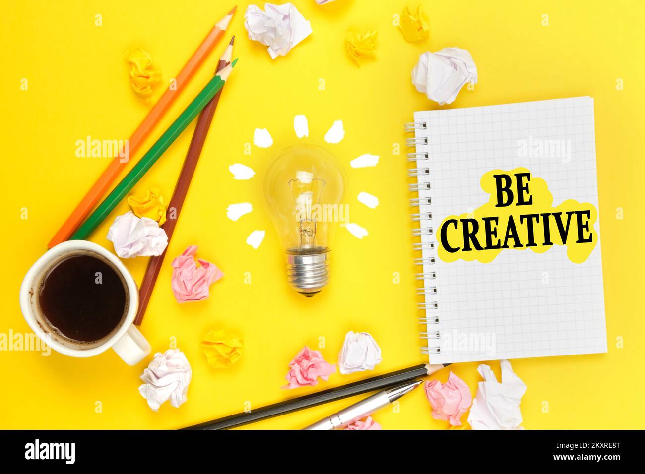 Concetto di business e di istruzione. Su uno sfondo giallo, una tazza di caffè, una lampadina, matite, un notebook con l'iscrizione - SIATE CREATIVI Foto Stock