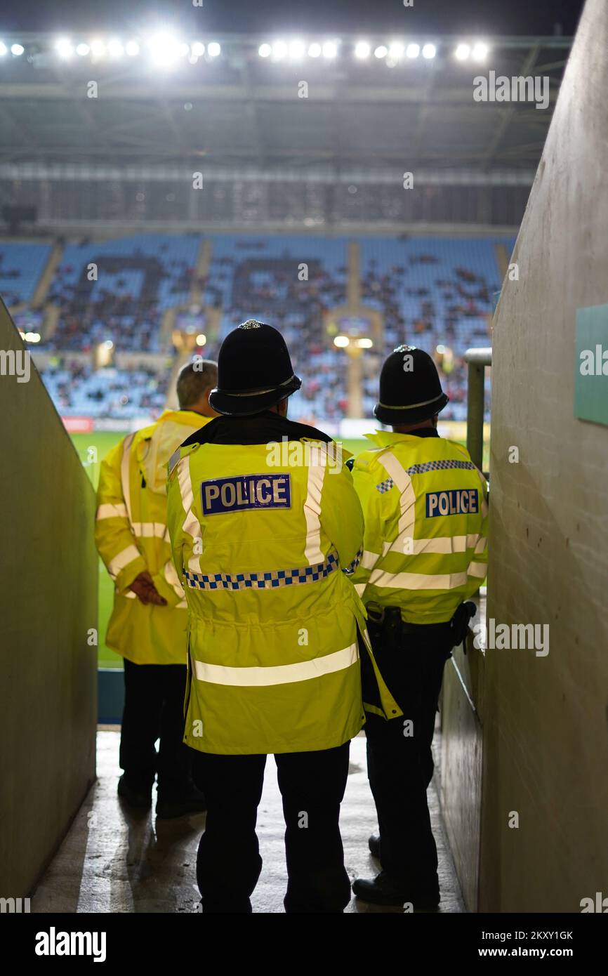 Gli agenti di polizia in alta visibilità, nella foto da dietro, guardano una partita di rugby da una scala Foto Stock