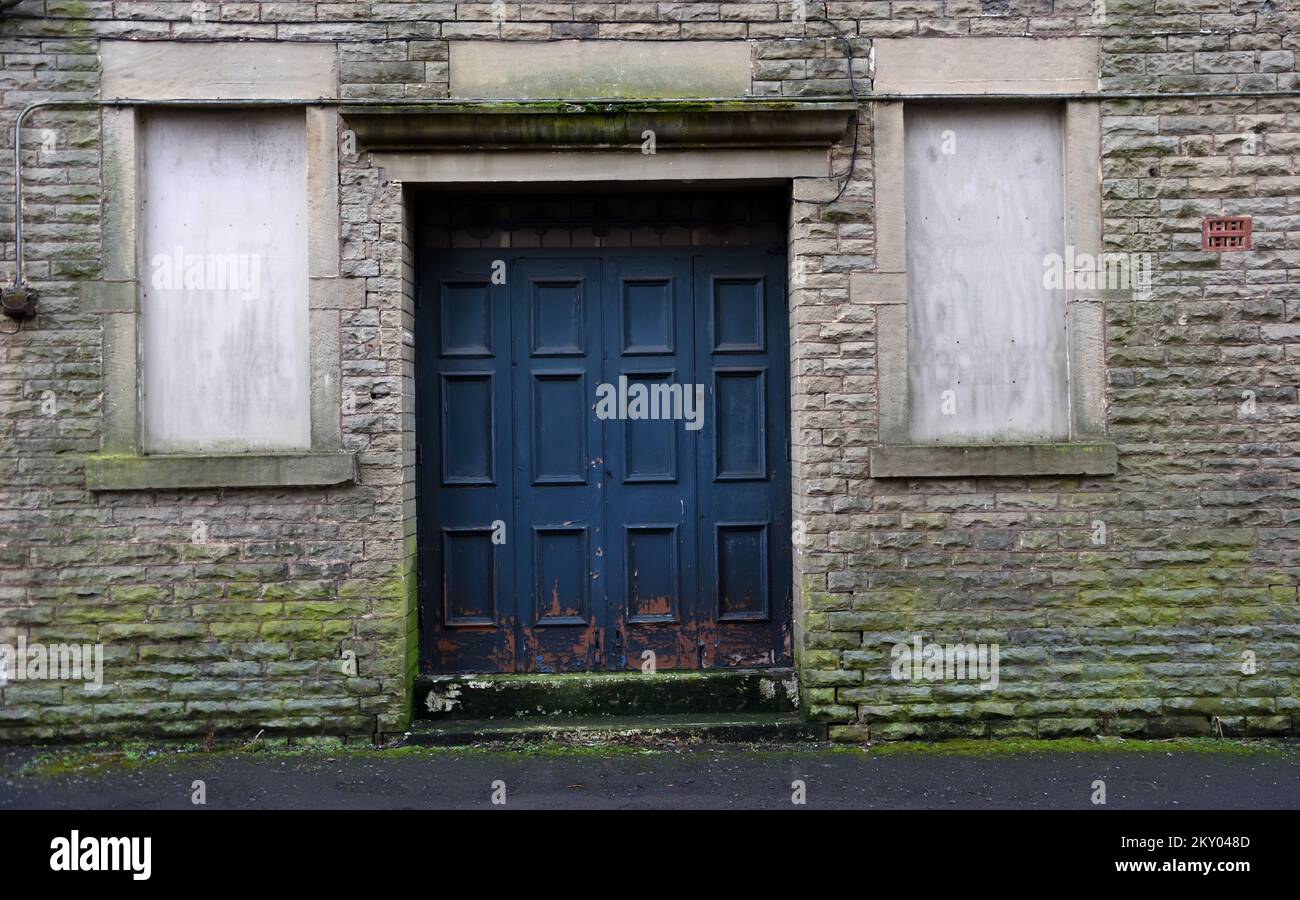 Porta blu vecchia e logora con vernice scagliante nella porta dell'edificio fronteggiato in pietra con finestre a bordo e muschio coperto. Ingresso alla vecchia danza Foto Stock