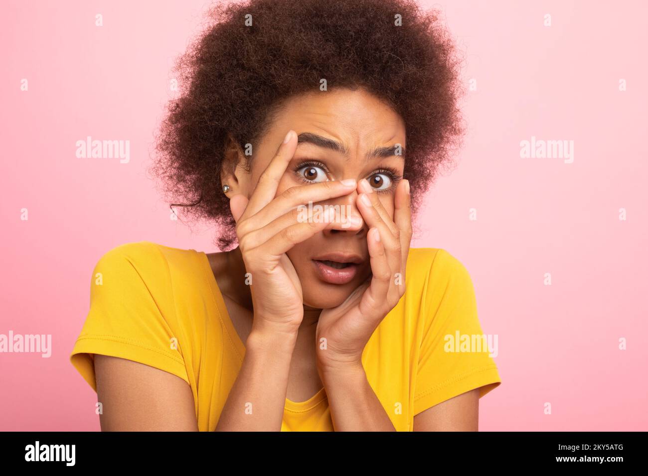 Paurito giovane studentessa afroamericana in t-shirt gialla che copre il viso con le mani e paura Foto Stock