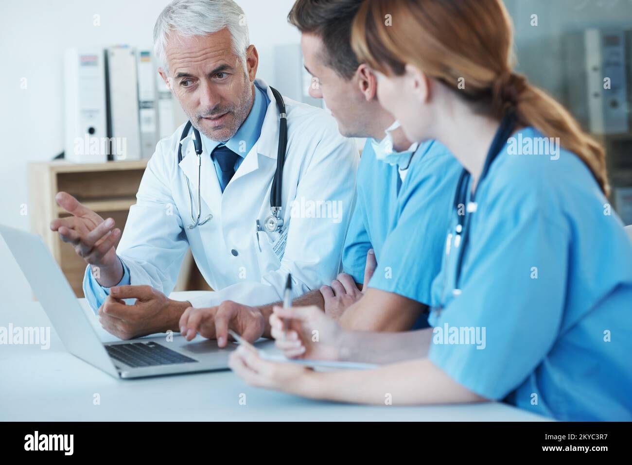 Questo è il modo in cui facciamo le cose. Tre medici che hanno una riunione e discutono le informazioni presentate su un portatile. Foto Stock