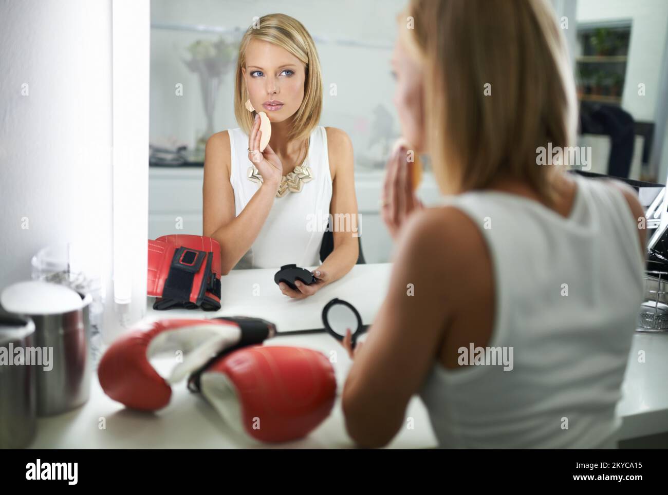 Theres più che incontra l'occhio. Una giovane donna alla moda che applica il make-up con un paio di guanti di boxe che si trovano accanto a lei. Foto Stock