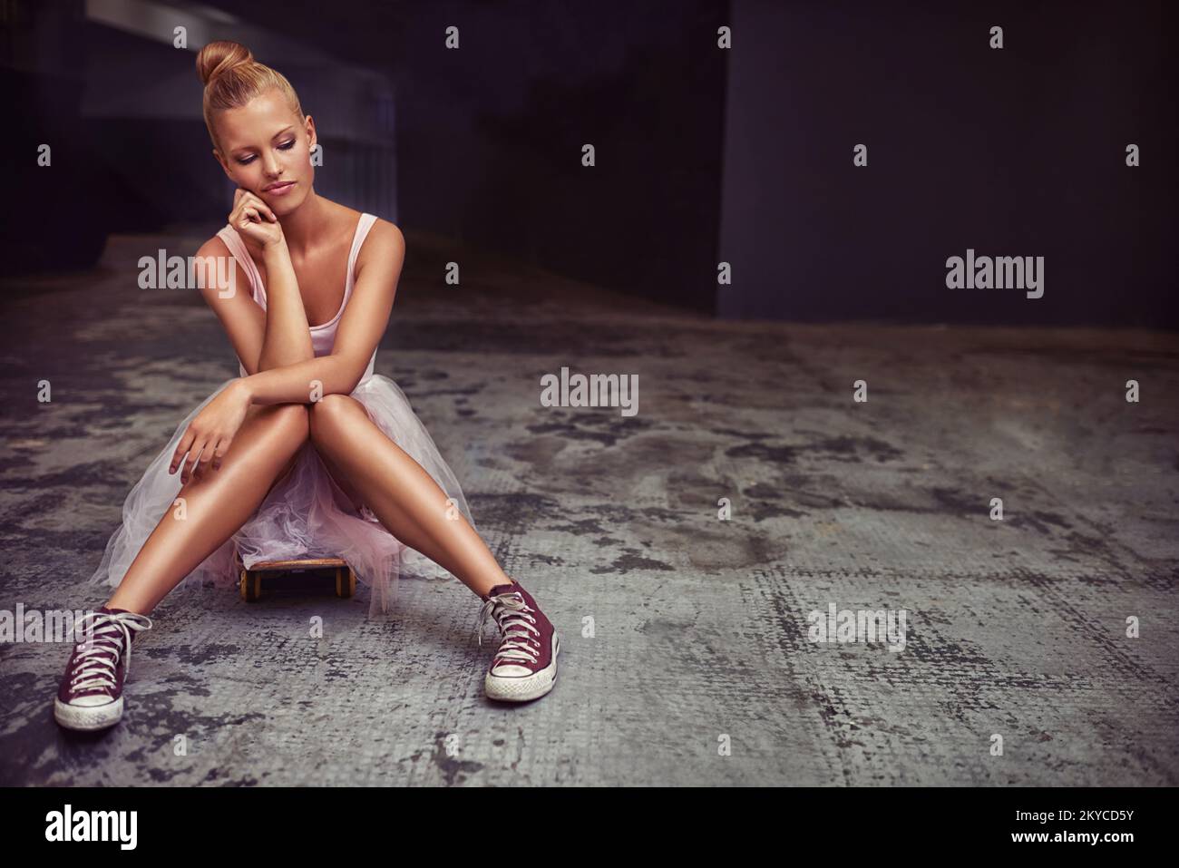 Ha molti lati alla sua personalità. Una giovane donna che indossa un balletto tutu e sneakers seduti su un pavimento di cemento. Foto Stock