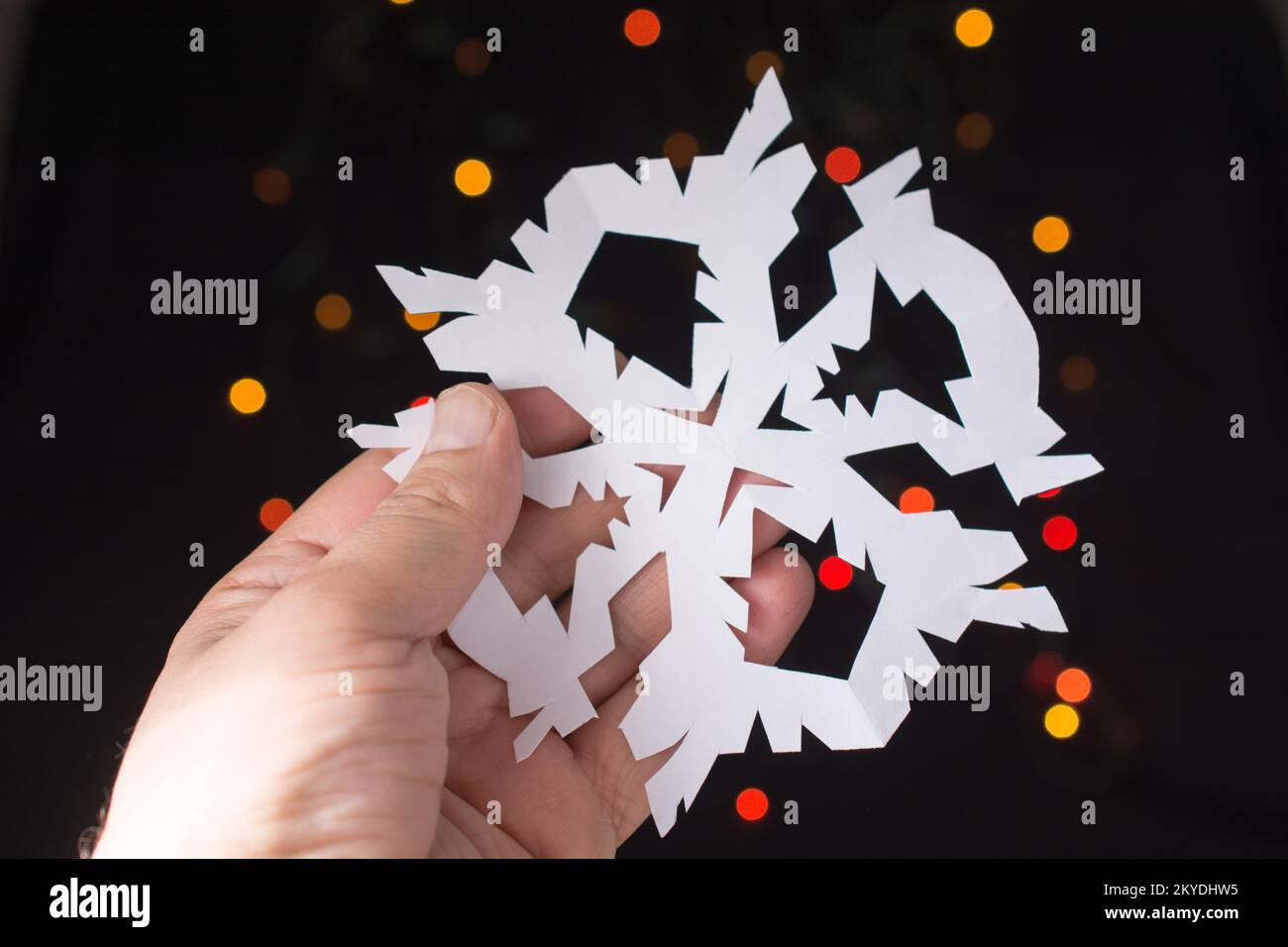 A forma di fiocco di neve con la carta in mano sul bokeh sfondo luminoso Foto Stock