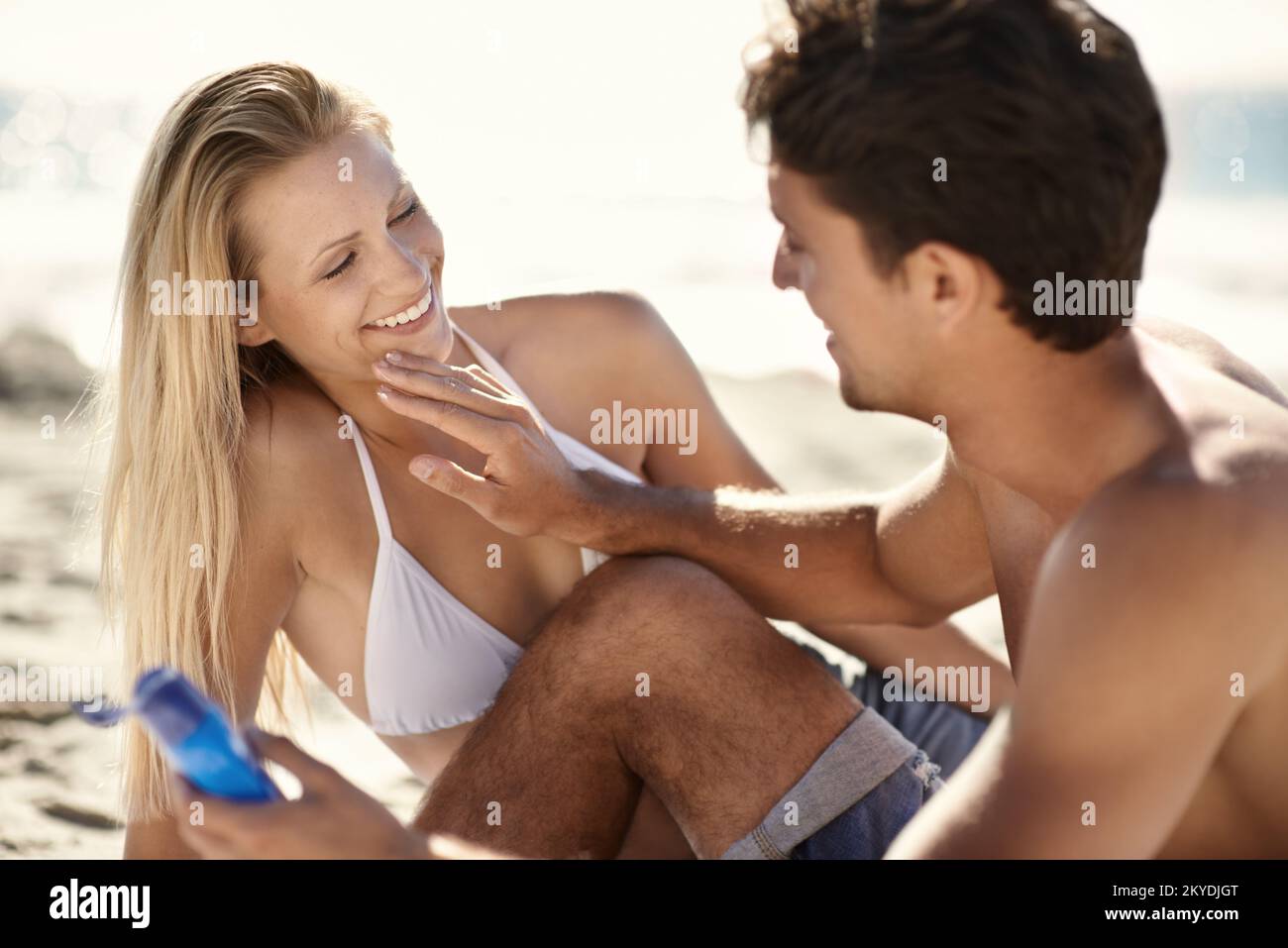 Divertimento con la crema solare. Una giovane coppia che applica crema solare in spiaggia. Foto Stock