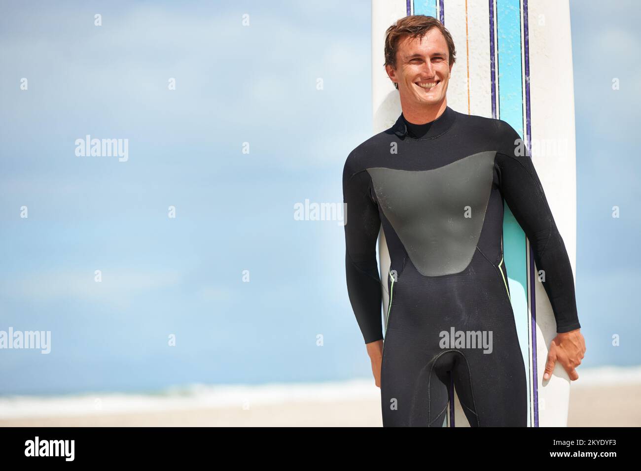Sono solo io e la mia tavola da surf. un surfista sorridente in piedi alla spiaggia con la sua tavola da surf. Foto Stock
