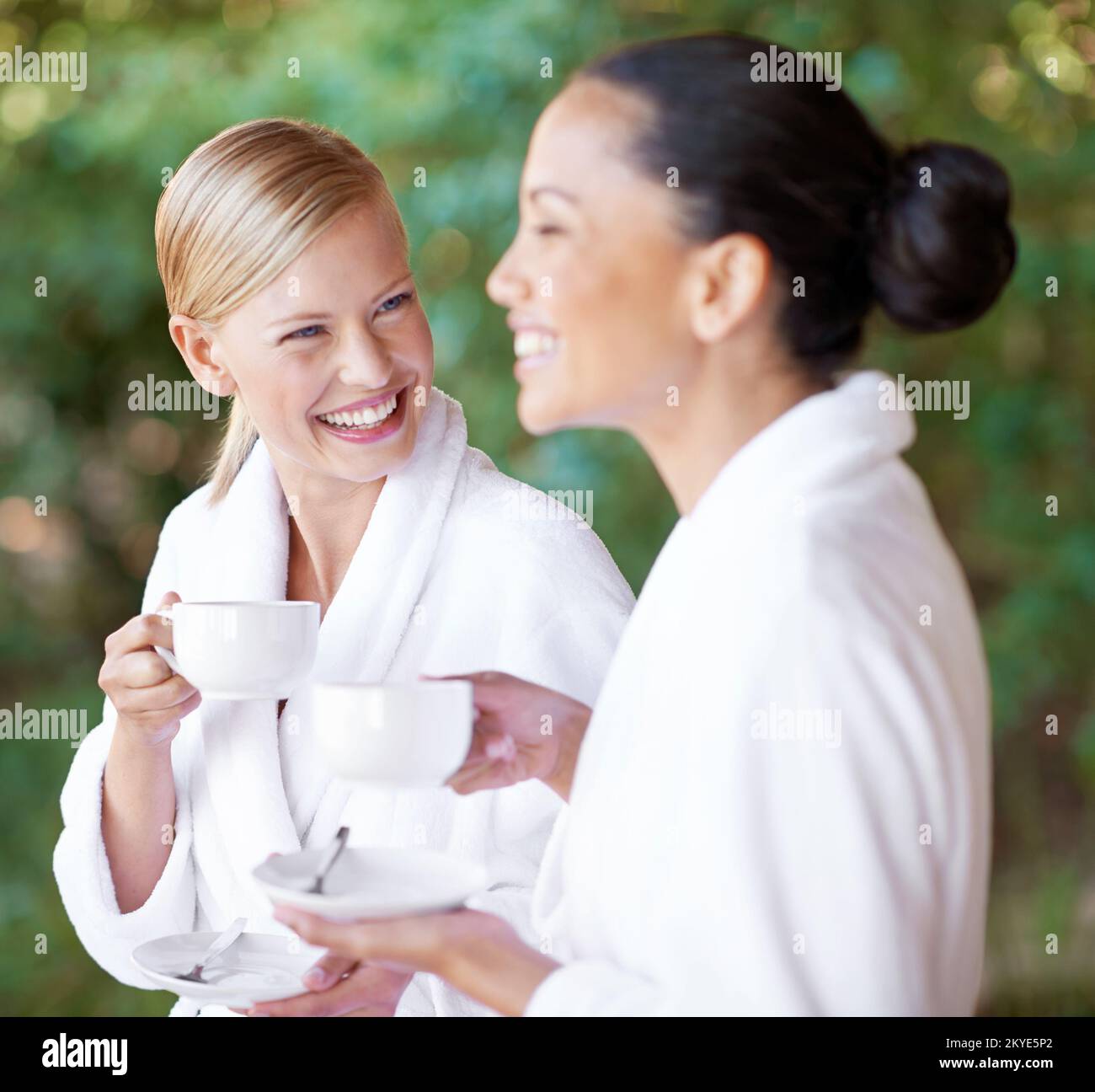 Fa questo gusto di tè alle erbe buon o che cosa. Due giovani donne che hanno un caffè negli accappatoi presso il centro benessere diurno. Foto Stock