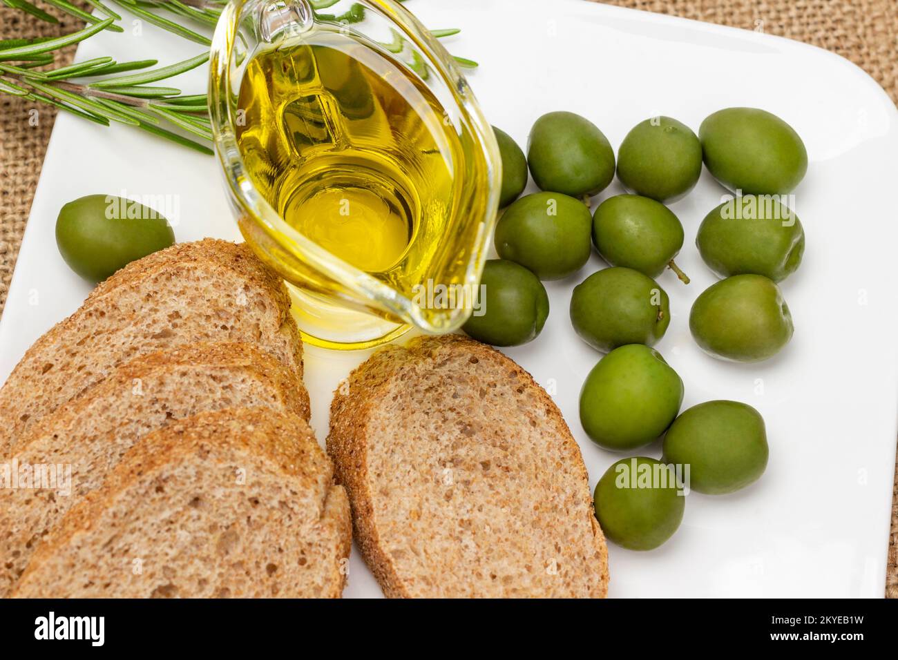 Olive verdi, una ciotola di olio d'oliva e baguette su un piatto bianco. Giacitura piatta Foto Stock