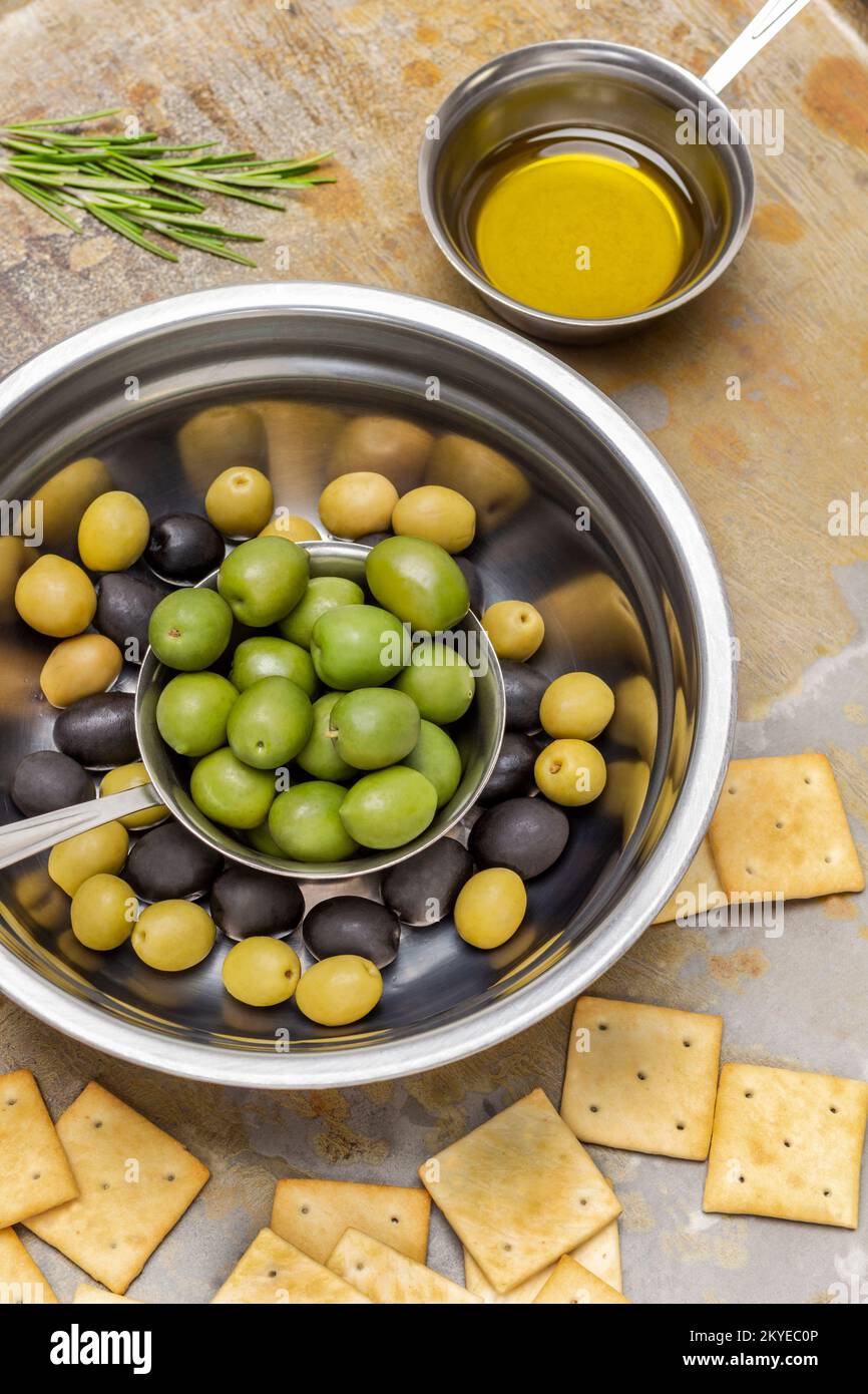 Olive nere e verdi in ciotole metalliche. Burro in una ciotola e biscotti sul tavolo. Fondo in metallo arrugginito. Giacitura piatta. Foto Stock