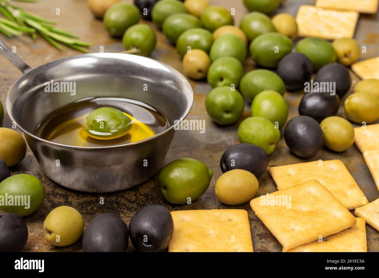 Olive nere e verdi, biscotti sul tavolo. Olio di oliva in una ciotola. Primo piano. Fondo in metallo arrugginito. Foto Stock