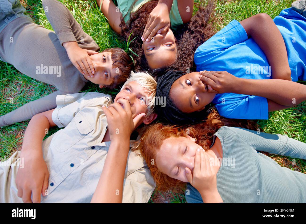 Potete mantenere un segreto. Un gruppo di bambini giacenti sull'erba coprendo la bocca. Foto Stock