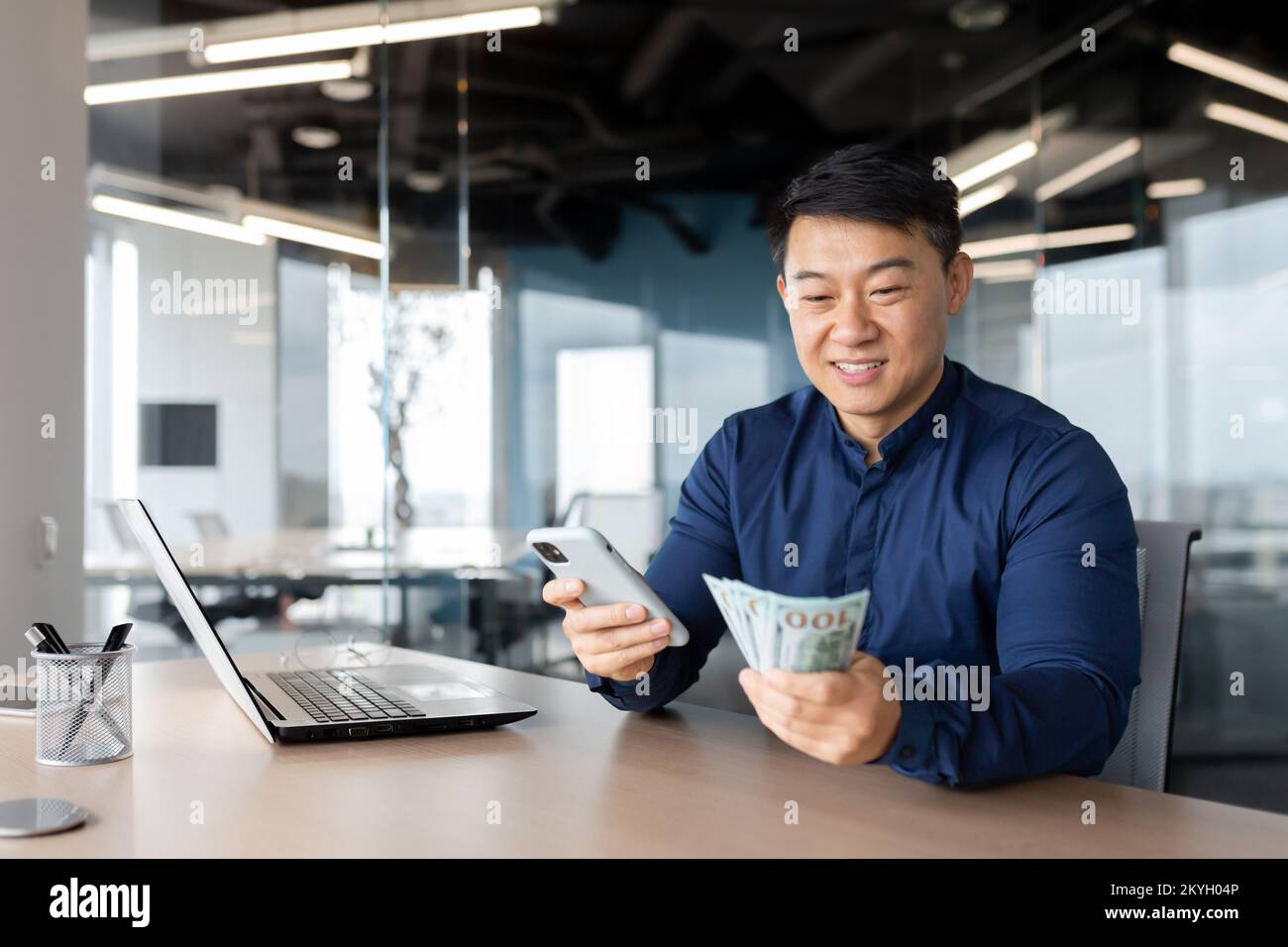 L'uomo d'affari asiatico ha vinto il dollaro, l'uomo seduto all'interno dell'ufficio che tiene contanti e telefono cellulare. Foto Stock