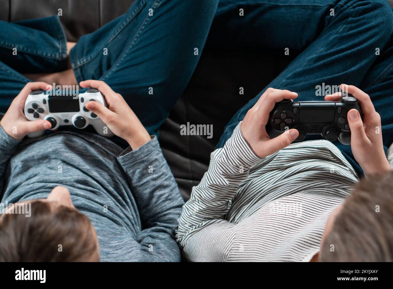 Mani di ragazzi seduti sul divano con joystick di gioco, dall'alto. I bambini giocano a videogiochi. I bambini in denim e casual longsleeves rilassarsi a casa Foto Stock