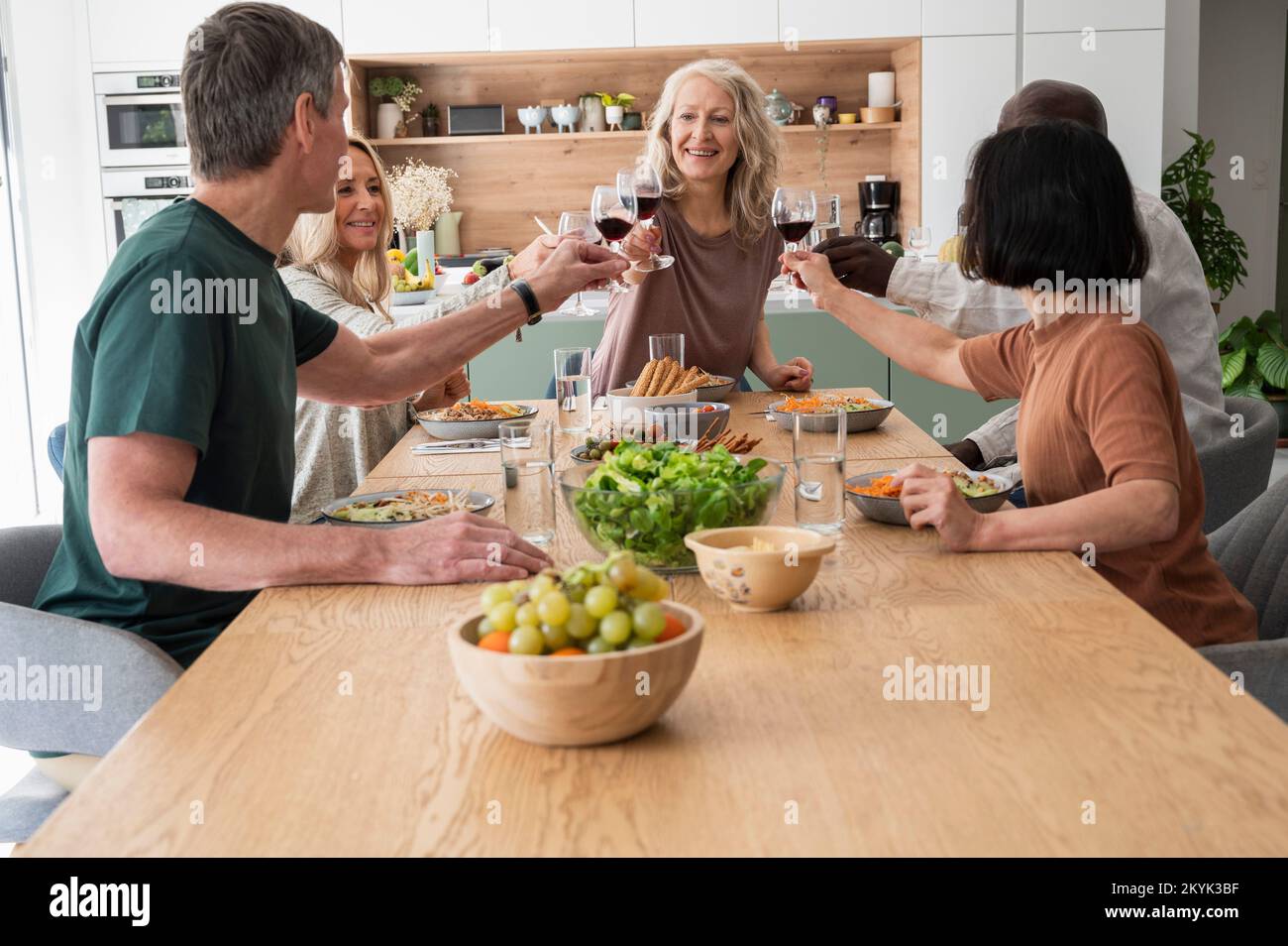 Group of diverse senior friends making a toast while having dinner at home Foto Stock