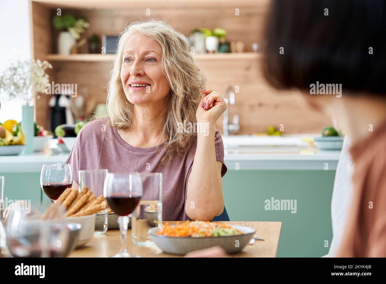 Foto di una donna matura seduta a tavola che si gode un pasto con gli amici Foto Stock